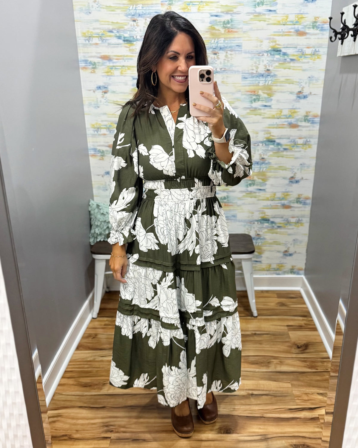 A woman takes a mirror selfie wearing a long-sleeve olive green maxi dress with a white floral print. The dress features a V-neckline, smock waist.