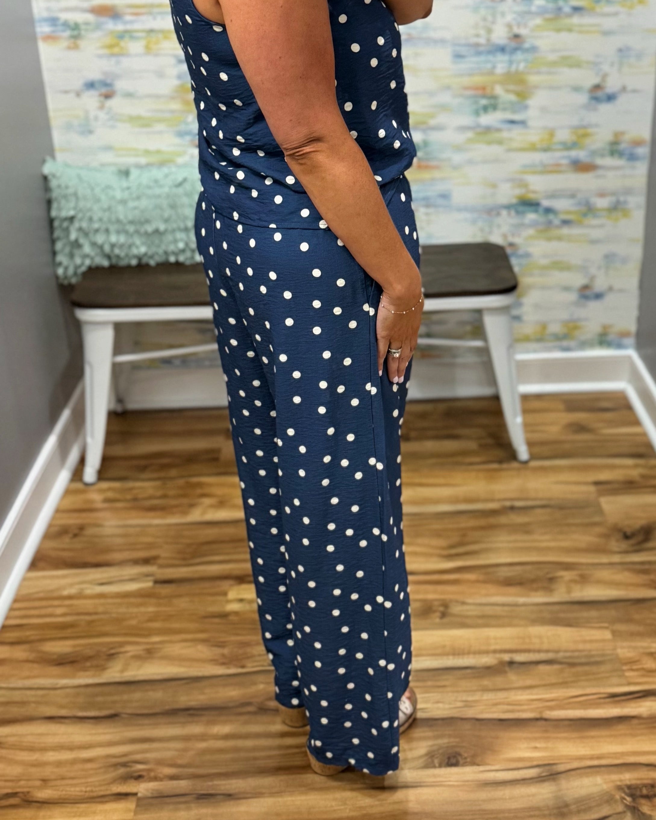 Person wearing a navy blue jumpsuit with white polka dots in a room with wooden flooring and a colorful wall.