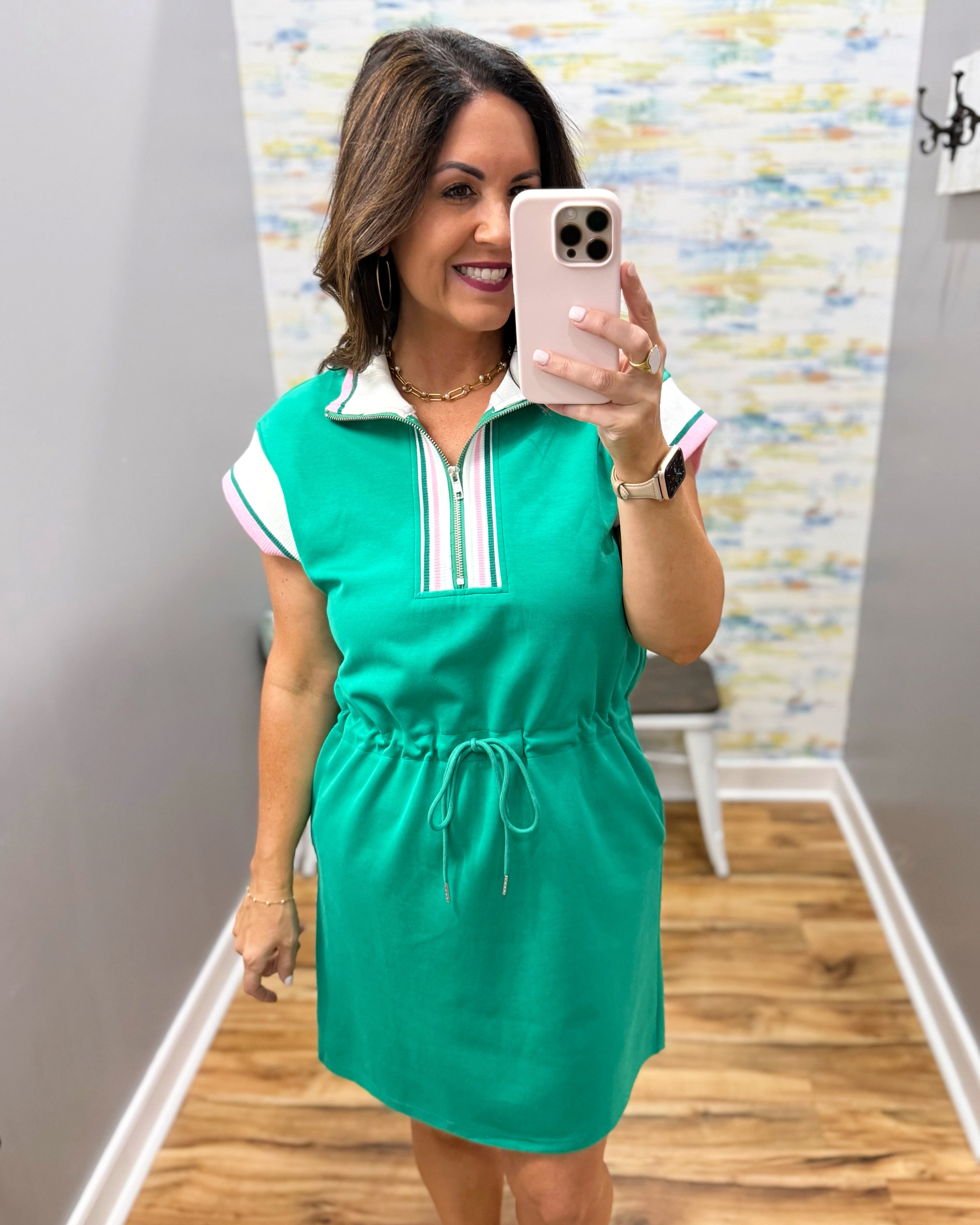 Woman taking a mirror selfie wearing a green dress with white and red accents.