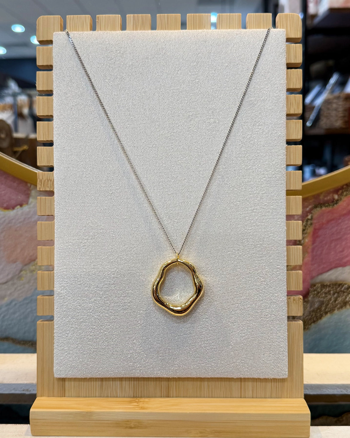 This two tone open ring pendant necklace features a sculpted organic wavy ring in polished gold tone hanging from a silver tone curb chain with a lobster clasp.