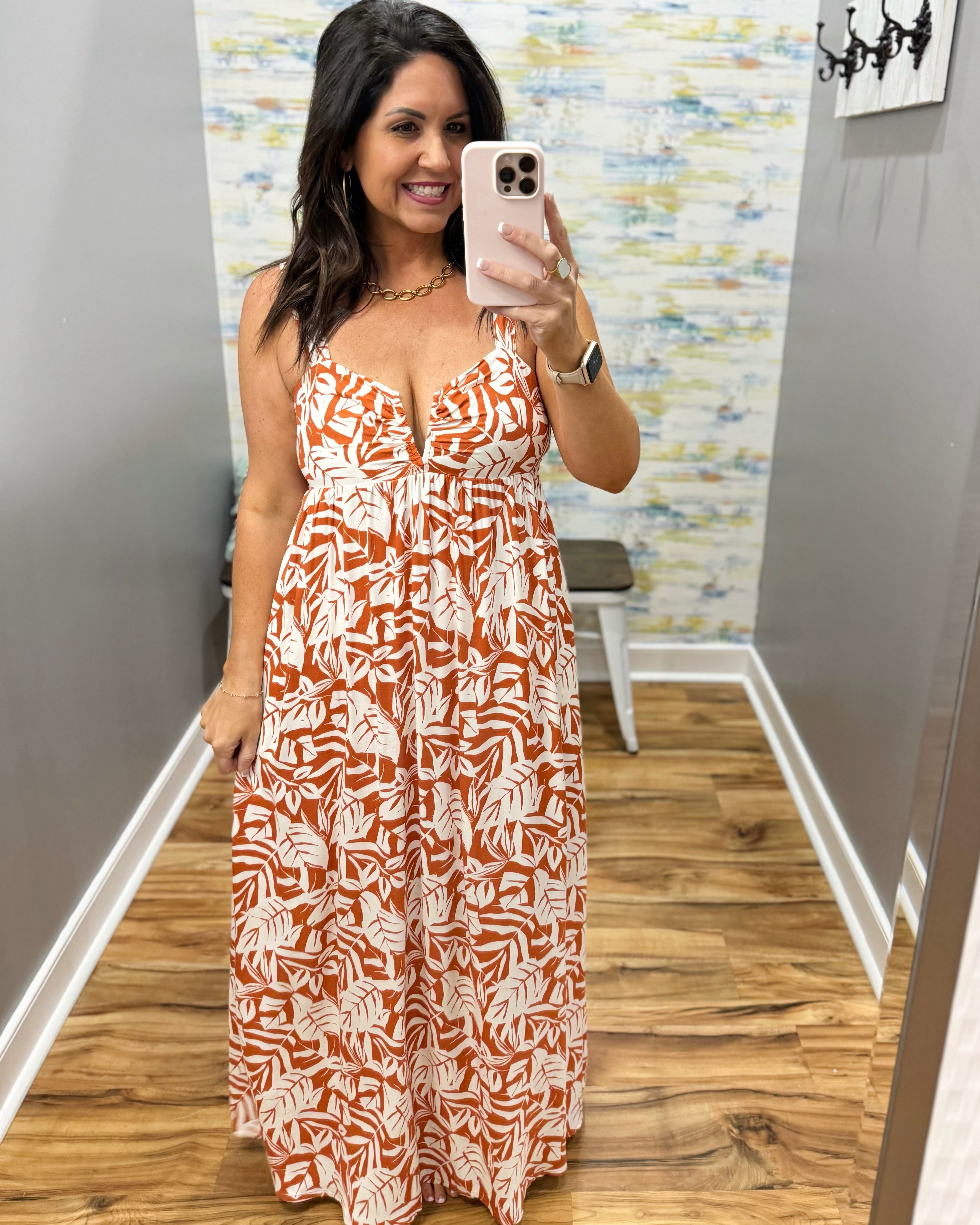 Woman taking a mirror selfie wearing an orange and white patterned dress in a room with wooden flooring and a colorful wall.