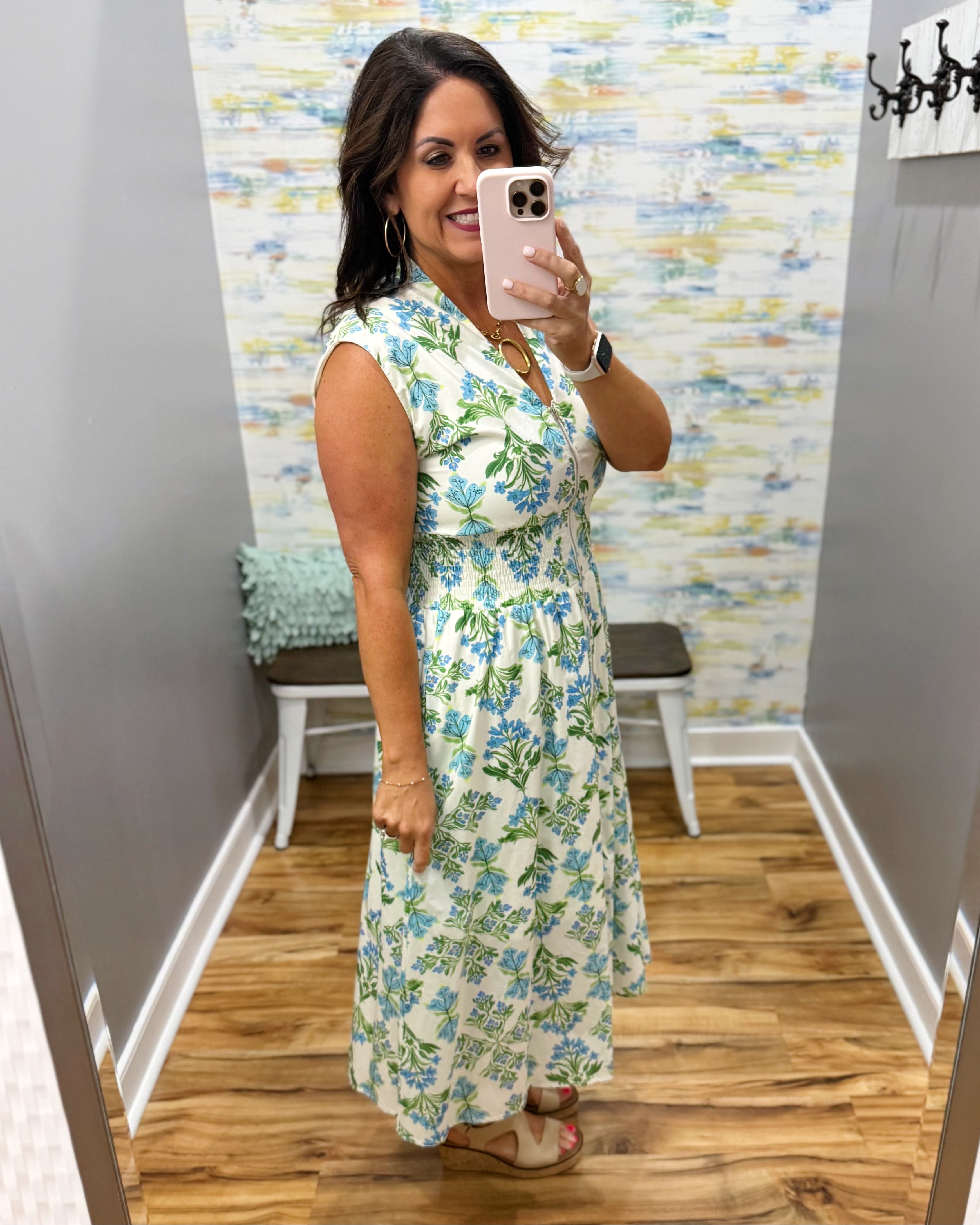 Woman taking a mirror selfie wearing a floral dress in a room with colorful striped wallpaper.