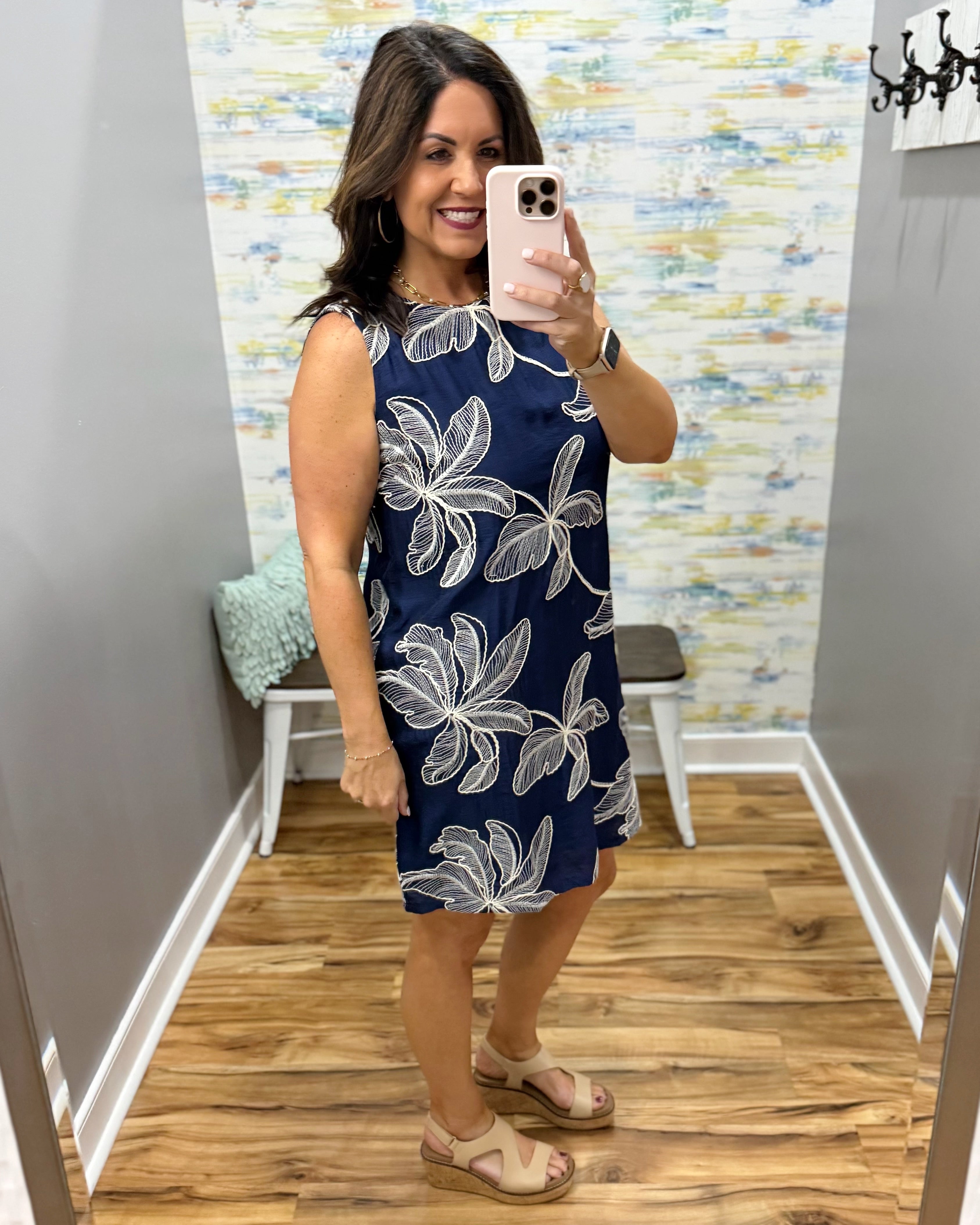 Woman taking a mirror selfie wearing a navy dress with white floral patterns in a room with a colorful wall.