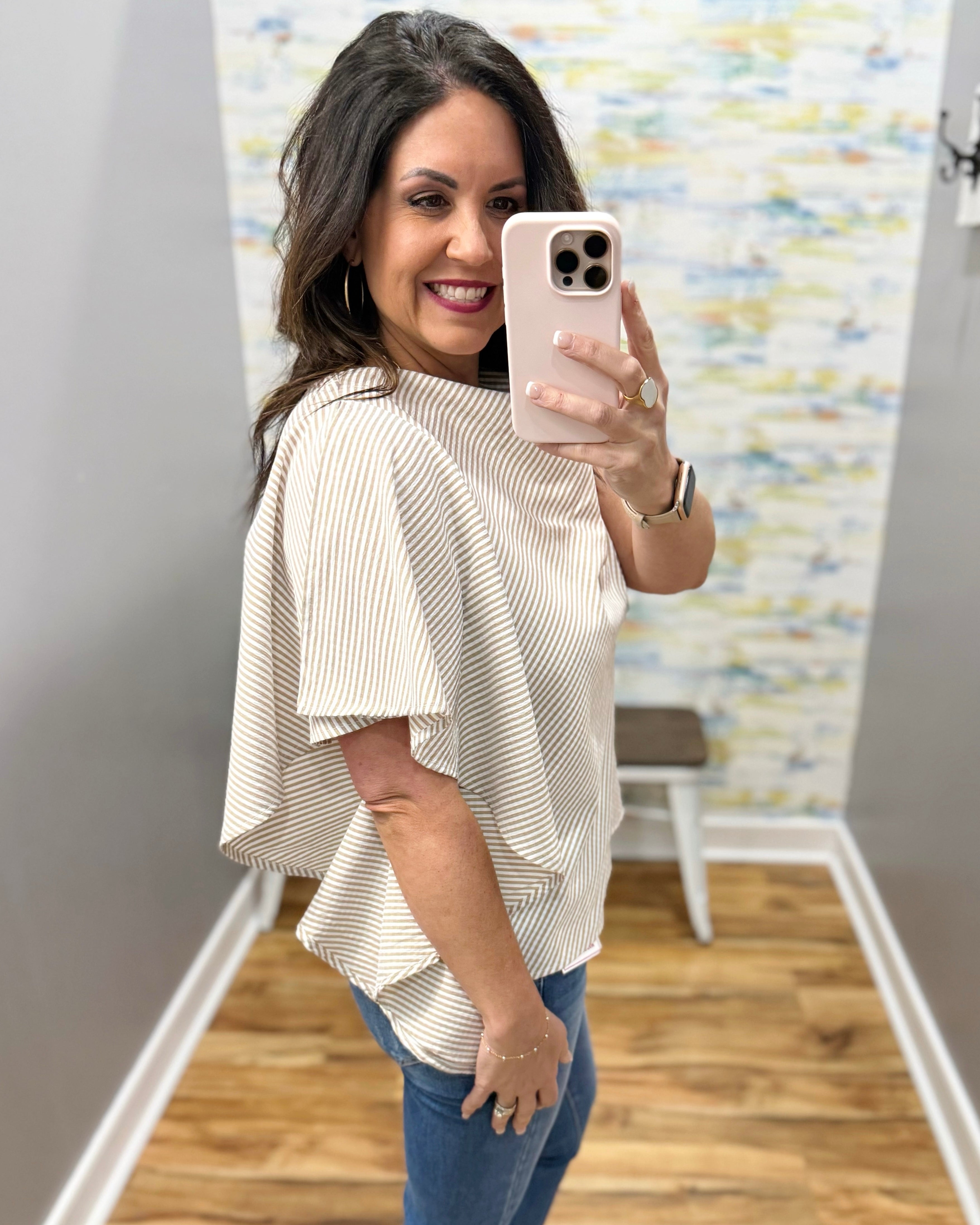 Woman taking a mirror selfie wearing a white blouse and blue jeans in a room with a colorful wall.