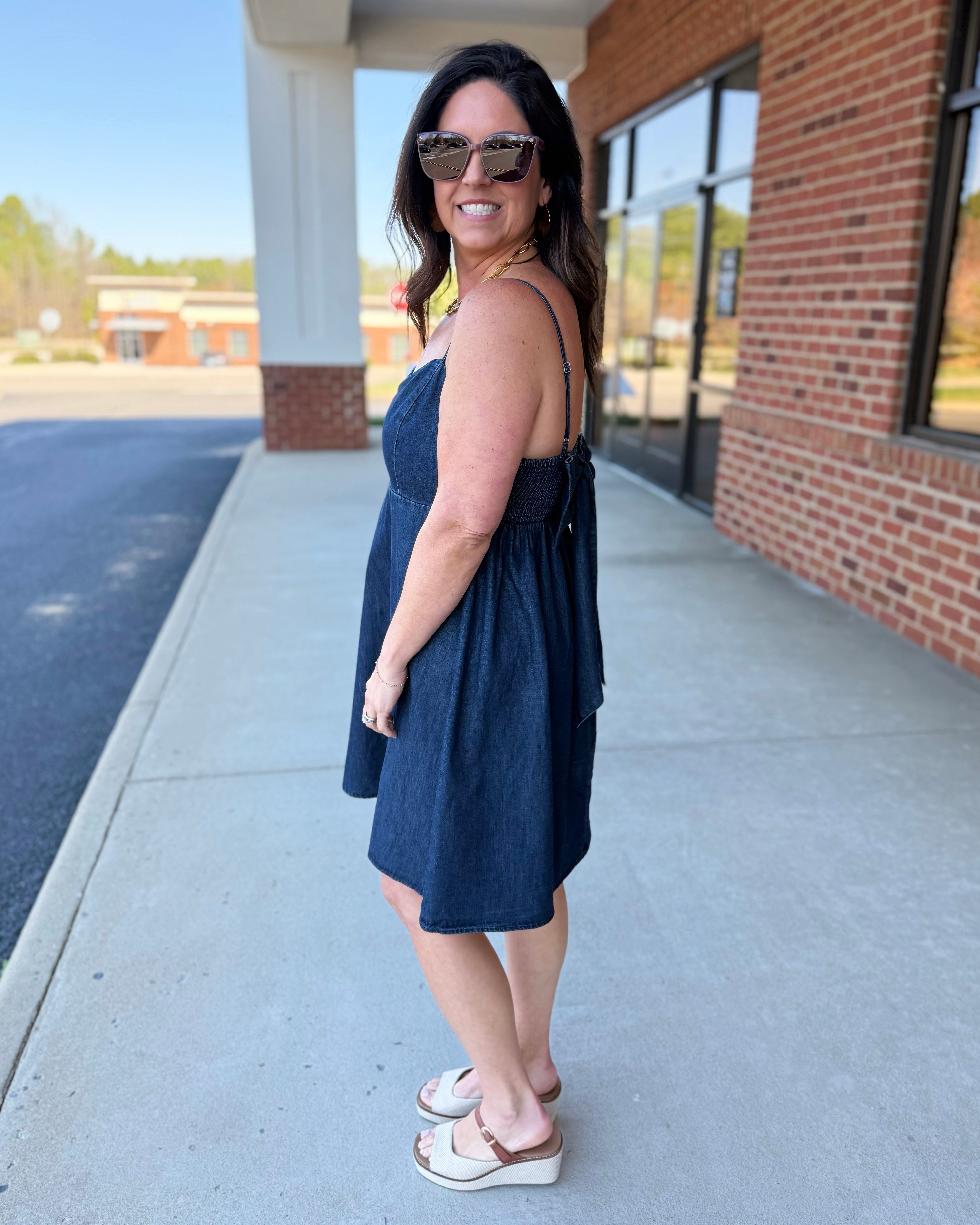 Woman in a navy dress standing on a sidewalk with a building in the background