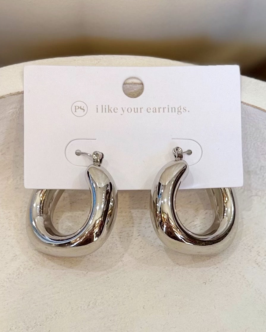 A pair of polished silver-tone hoop earrings displayed on a white branded card that reads 'i like your earrings.' The earrings have a reflective, smooth finish and are shown against a soft neutral background.