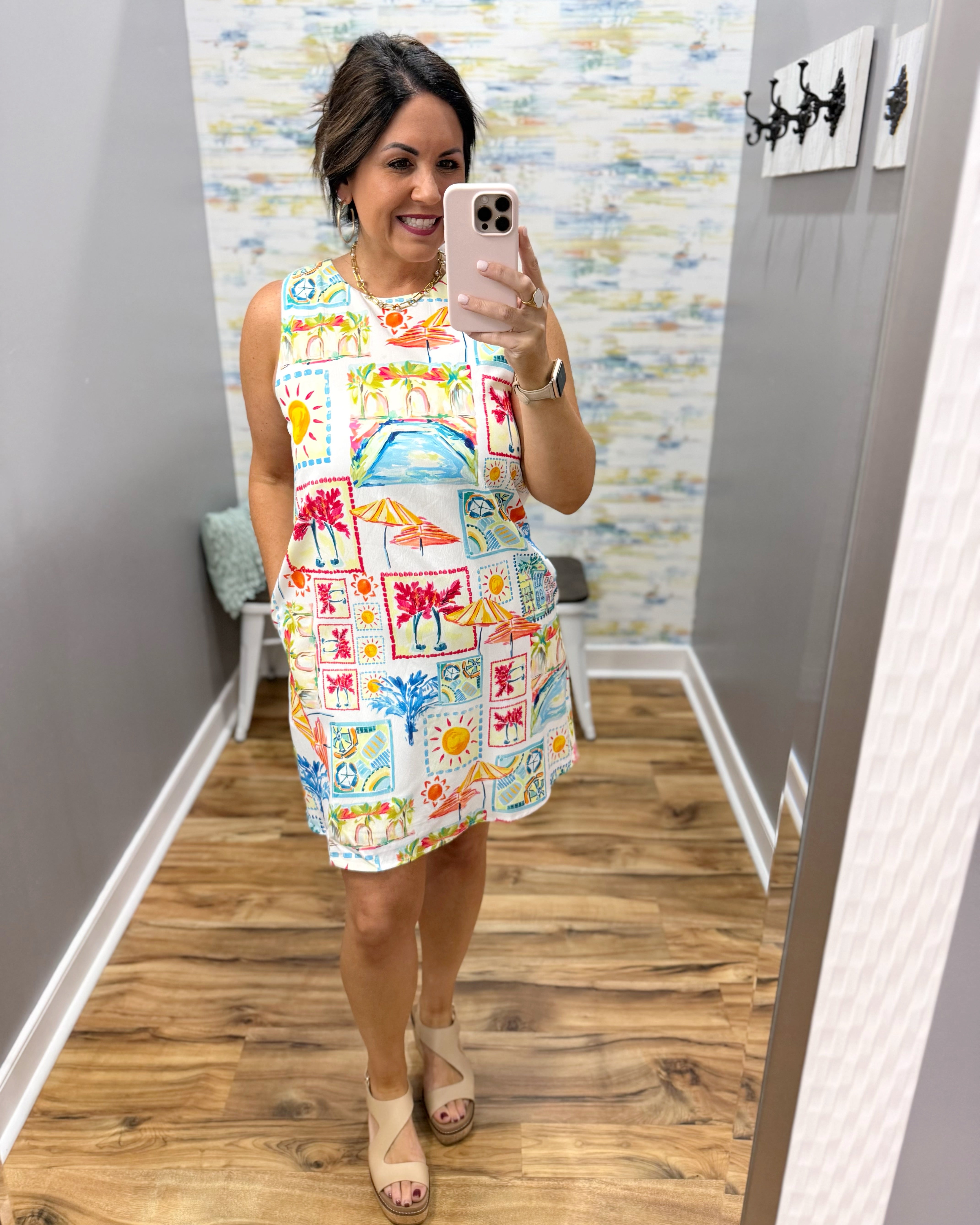 Woman taking a mirror selfie wearing a colorful dress with a pattern of cars and other designs.