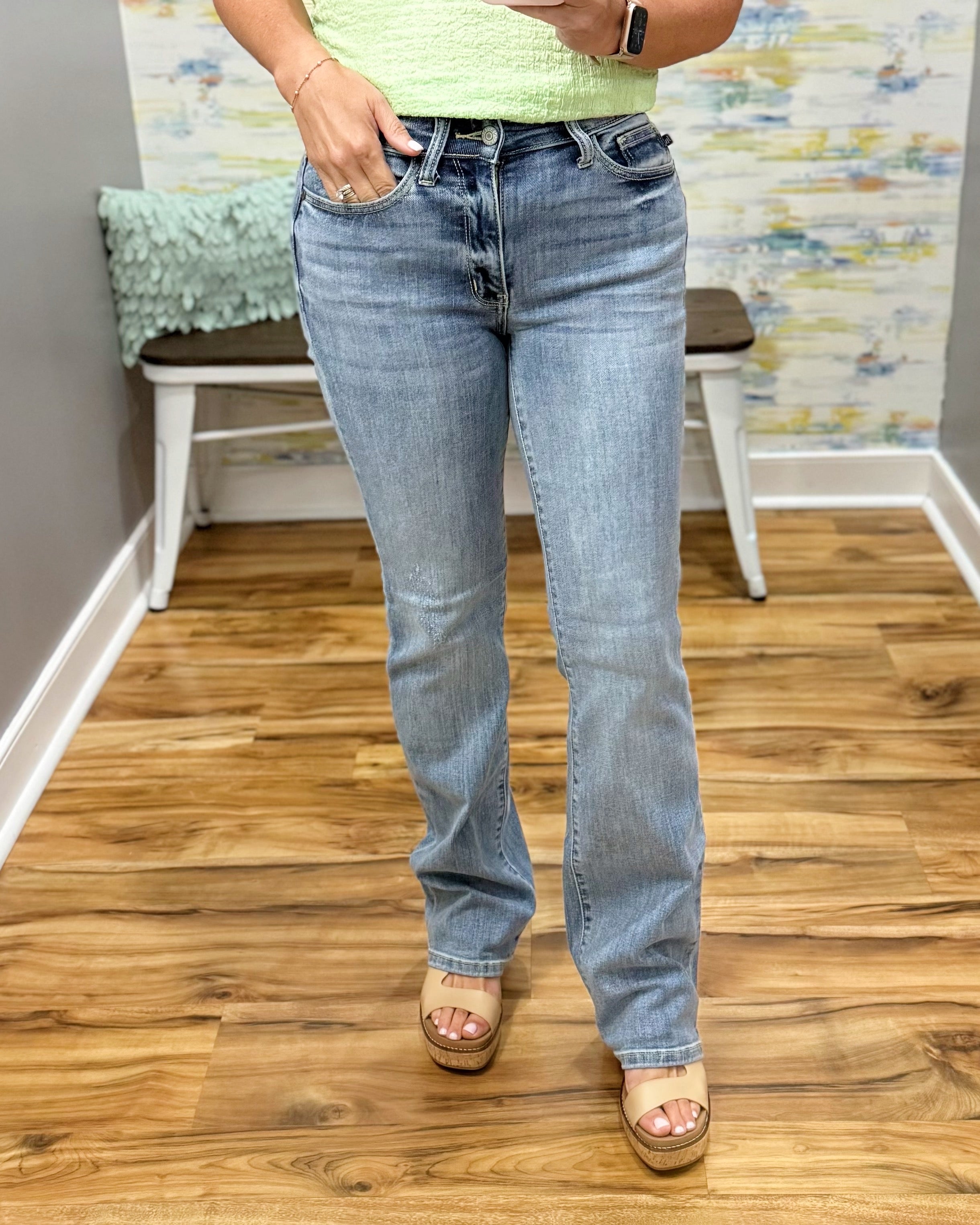 Person wearing light blue jeans standing on a wooden floor with a colorful wall in the background.