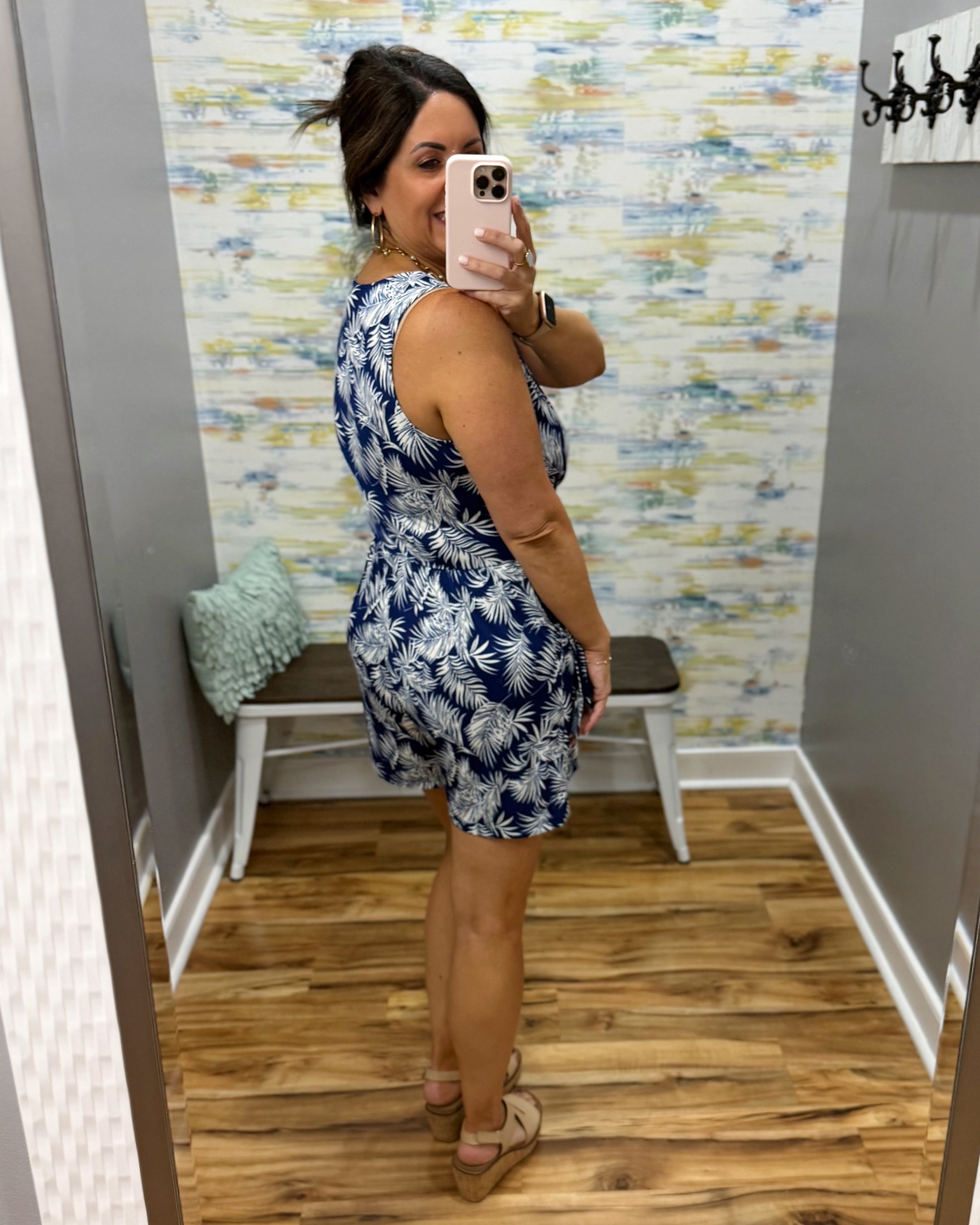 Woman taking a mirror selfie wearing a blue floral dress in a room with patterned wallpaper.