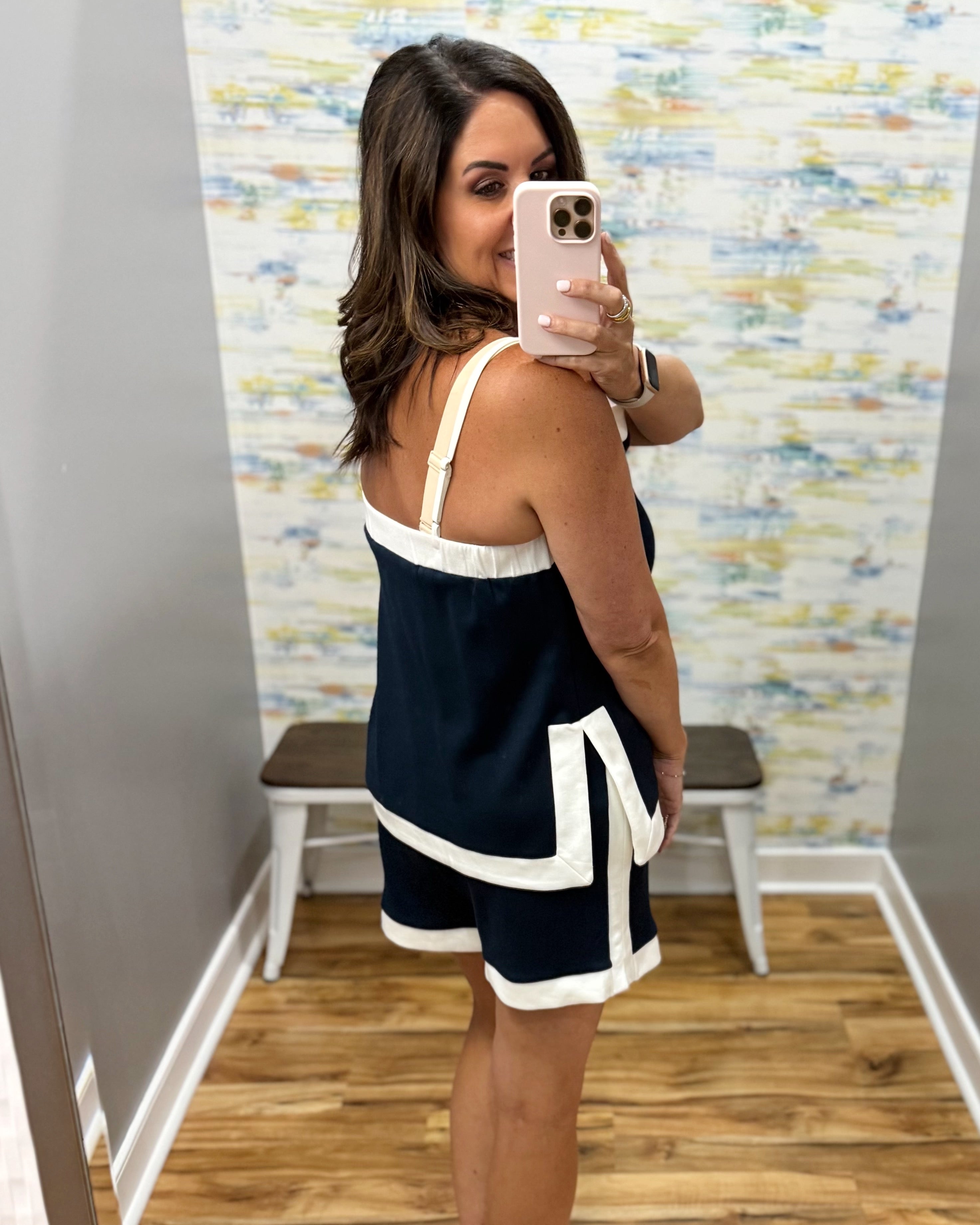 Woman taking a mirror selfie wearing a navy and white dress in a room with a colorful wall.