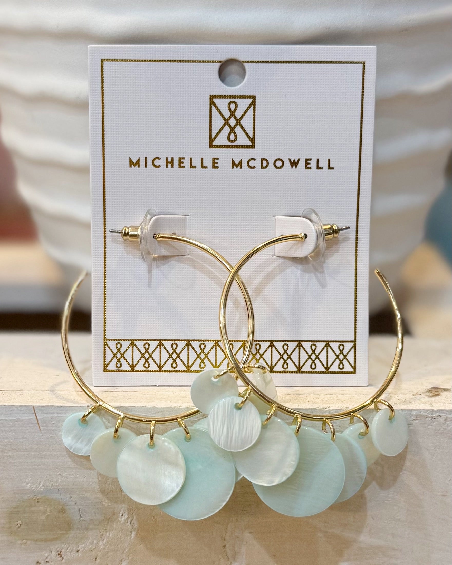 Gold hoop earrings with light green circular charms on a Michelle McDowell branded card.
