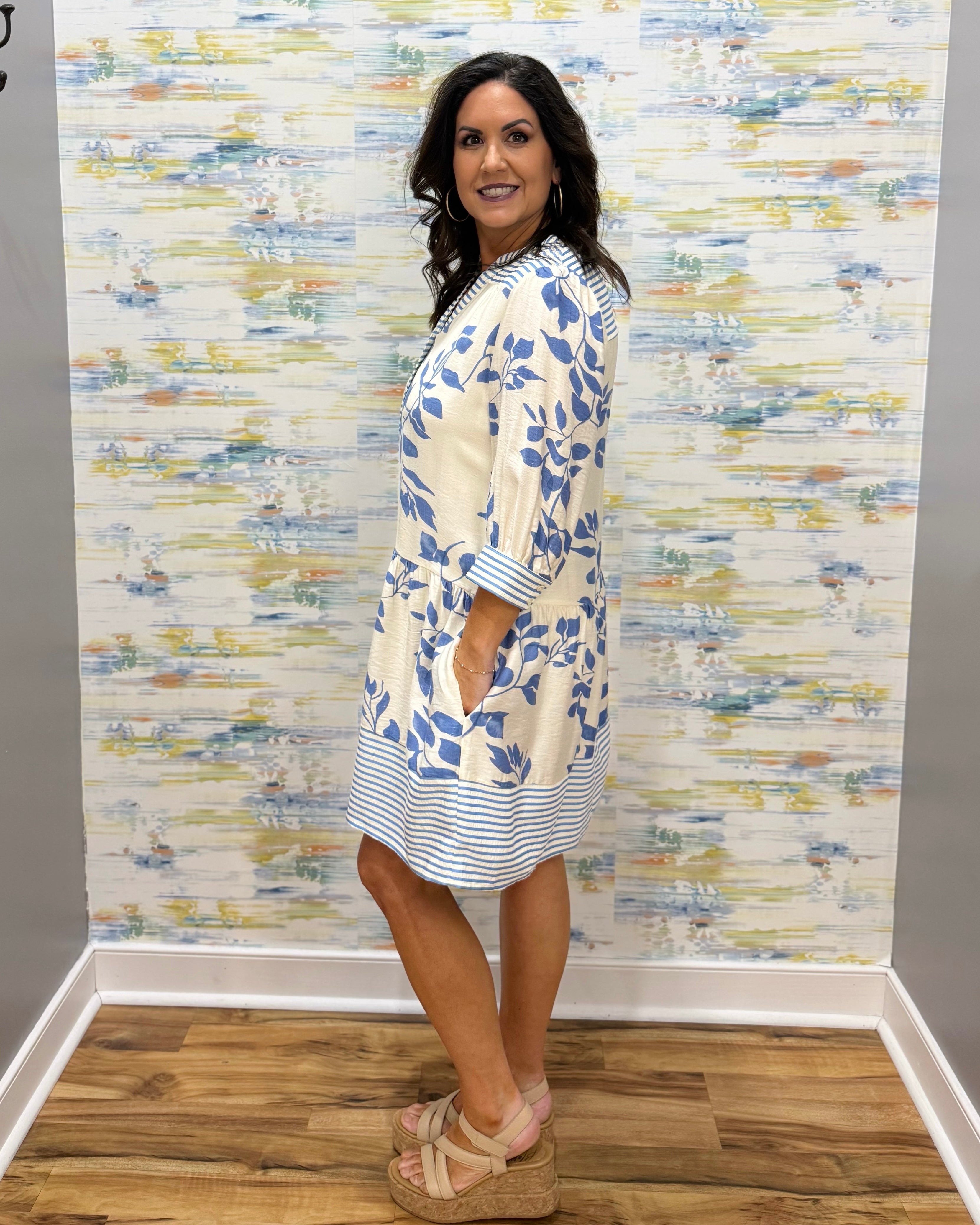 Woman wearing a floral dress standing against a textured wall.