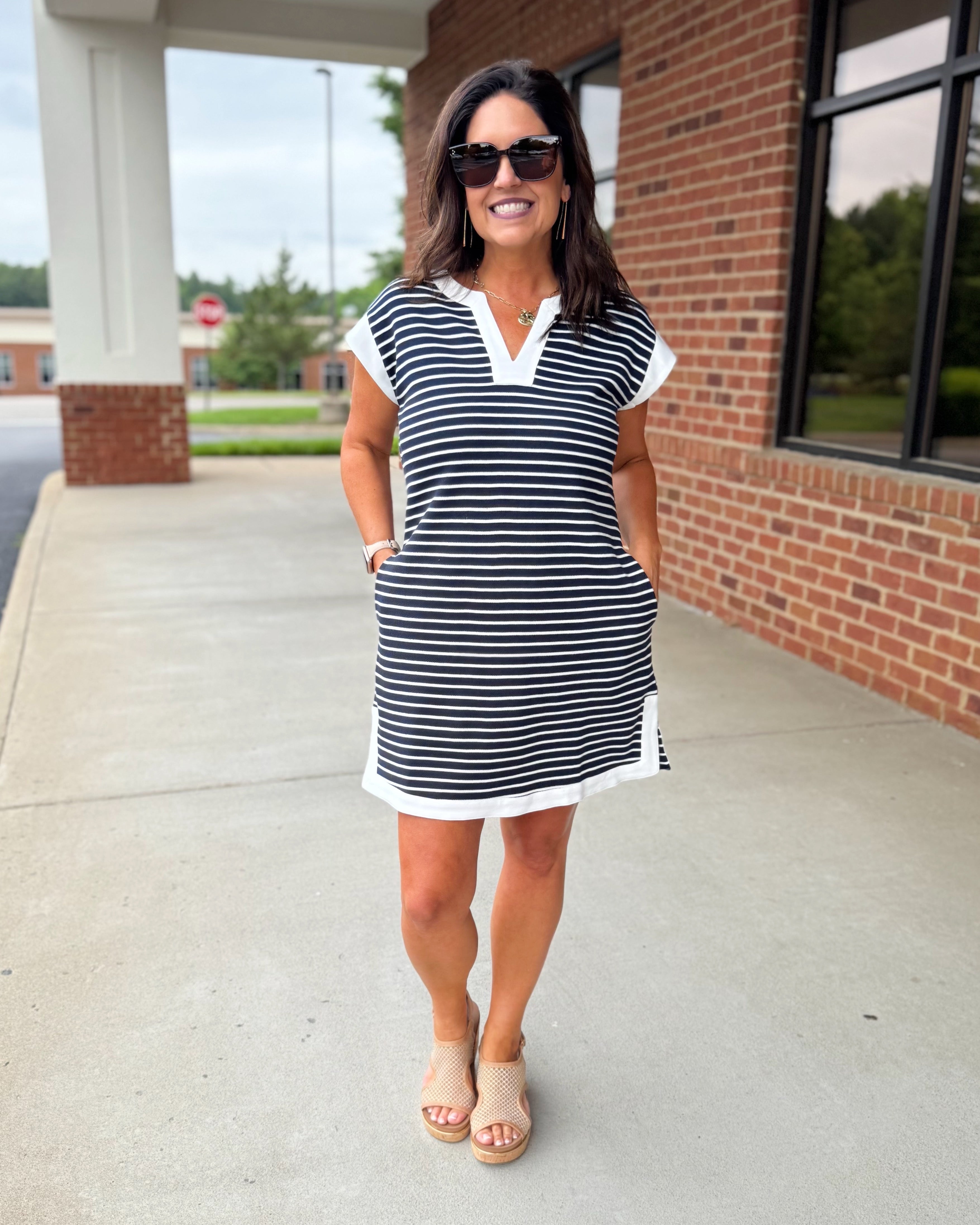 Woman wearing a navy and white striped dress standing on a sidewalk.