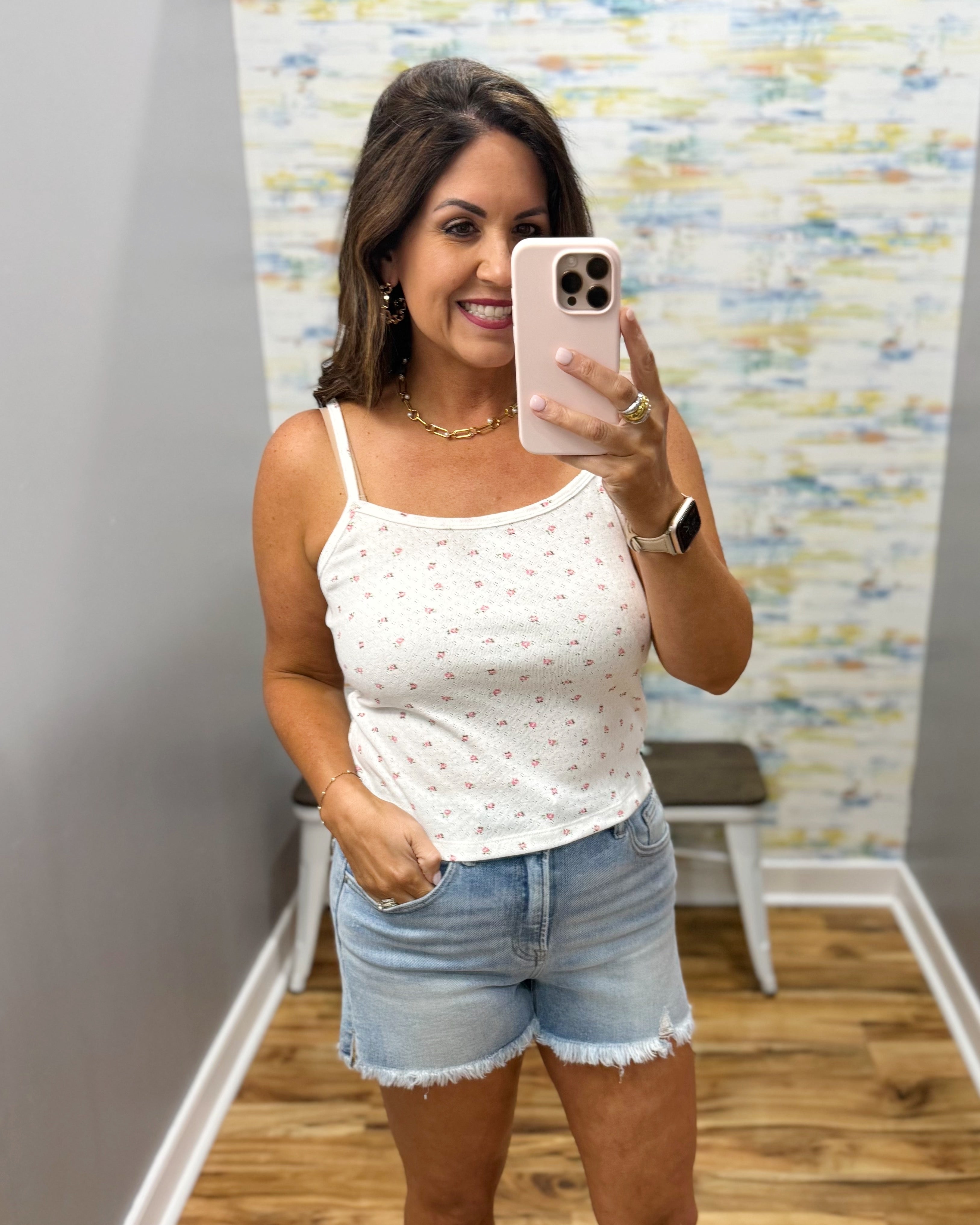 woman wearing white floral cami top with denim shorts.