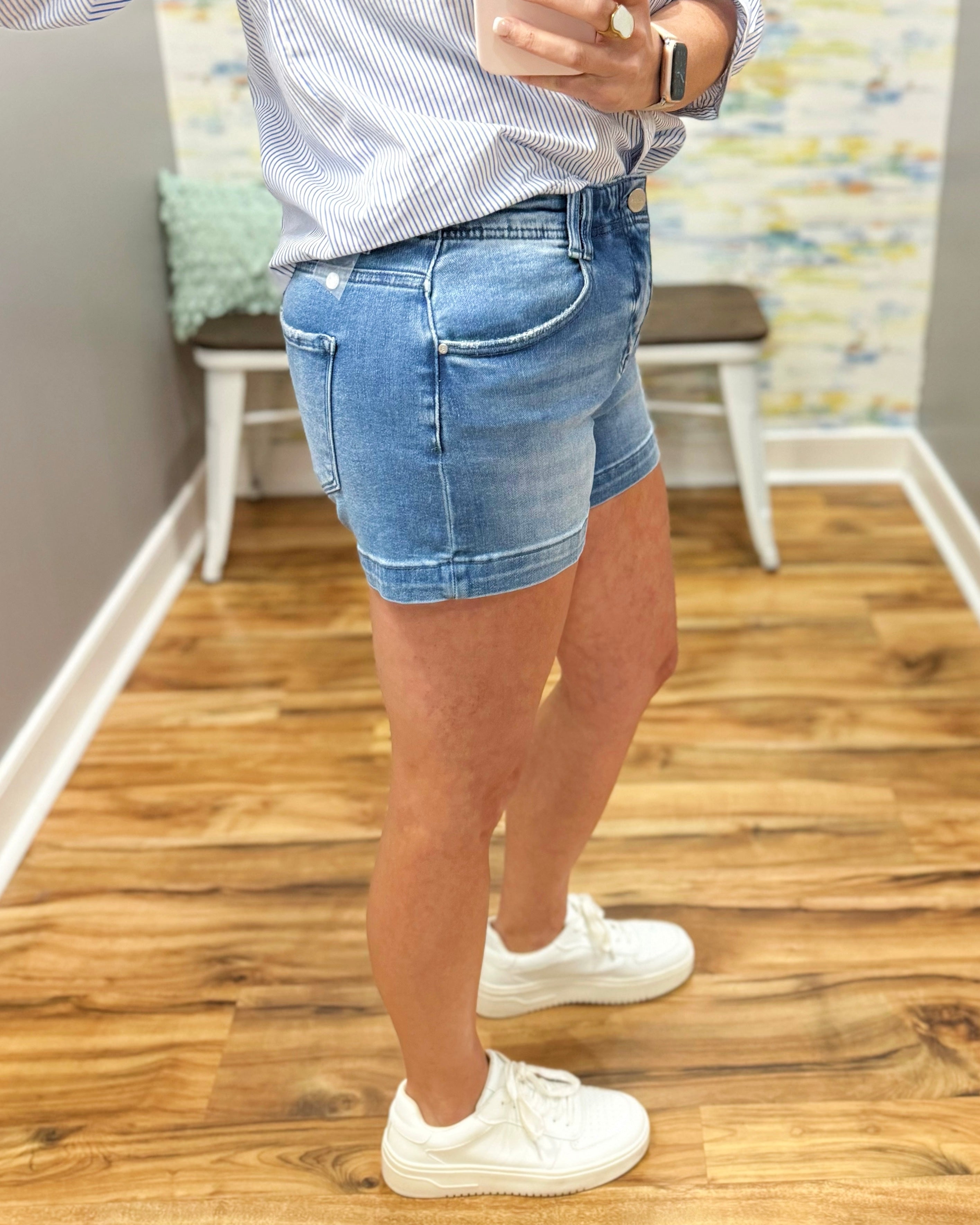 Person wearing blue denim shorts and white sneakers on a wooden floor.