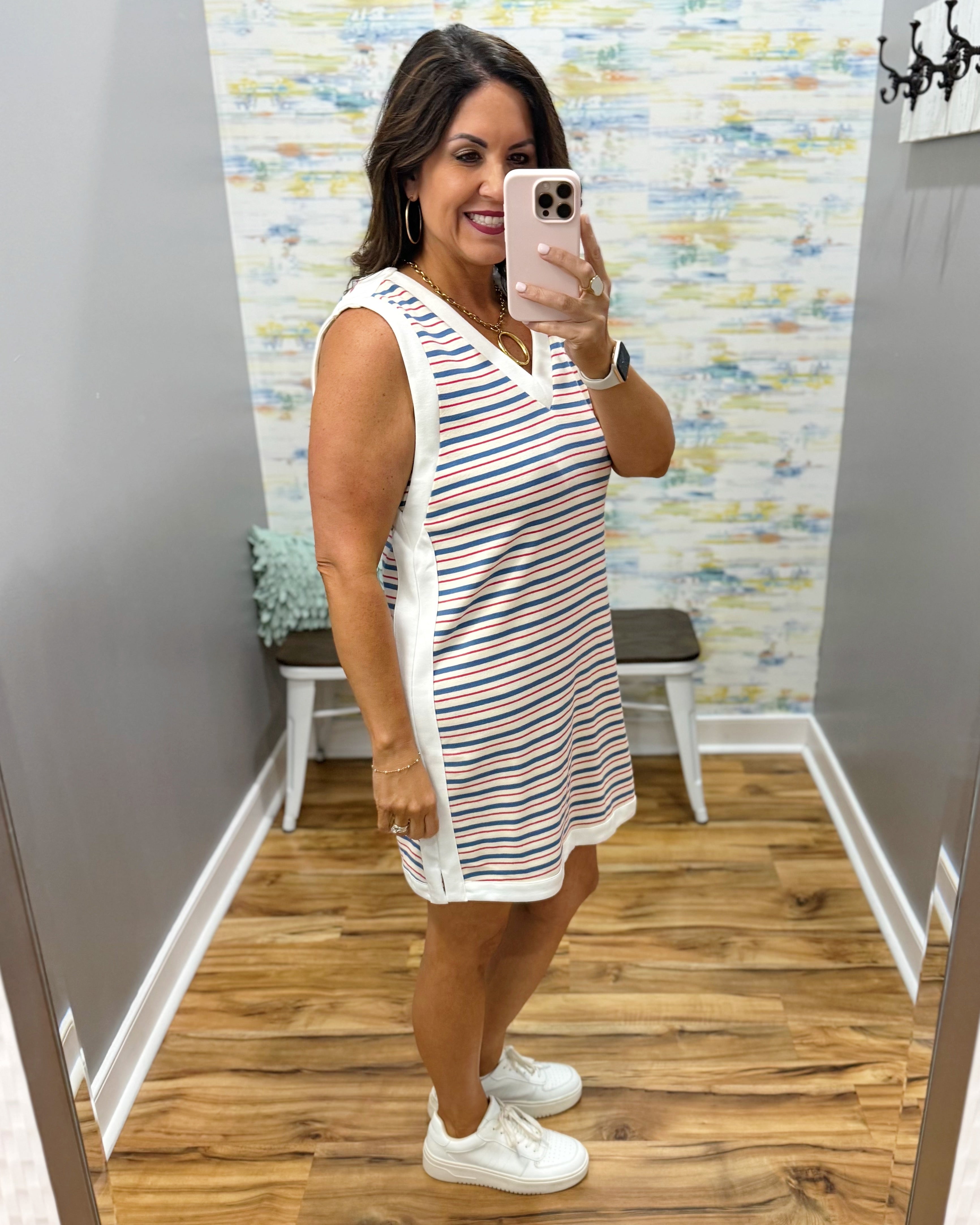Woman taking a mirror selfie wearing a striped dress and white sneakers in a store.