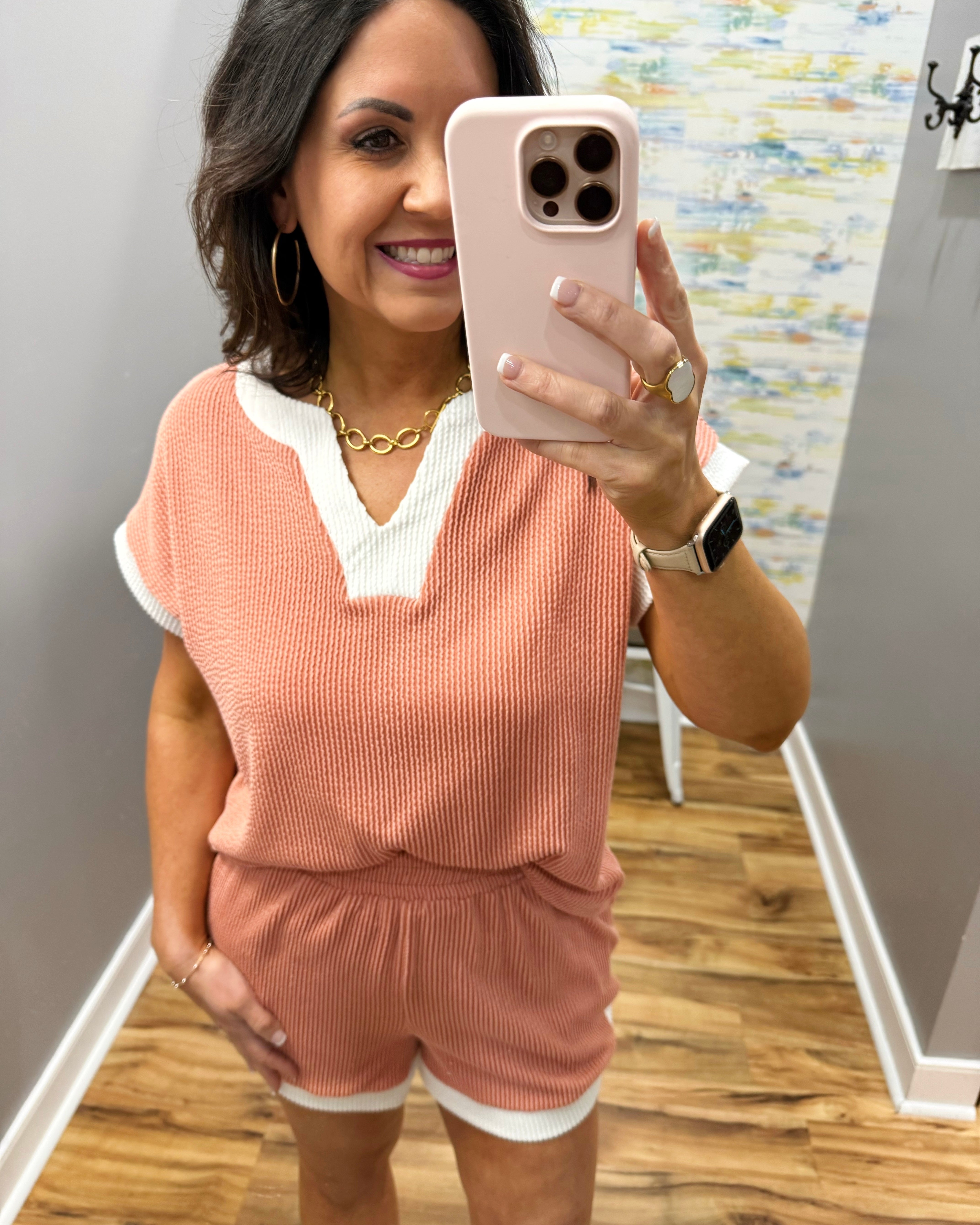 Woman taking a mirror selfie wearing a pink outfit with a white shirt underneath.
