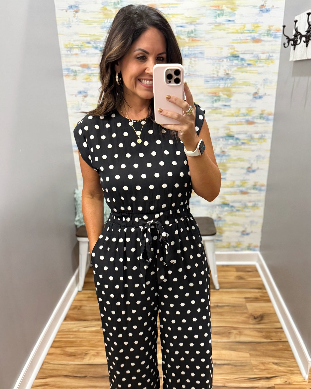woman taking a selfie wearing a black and white polka dot jumpsuit.