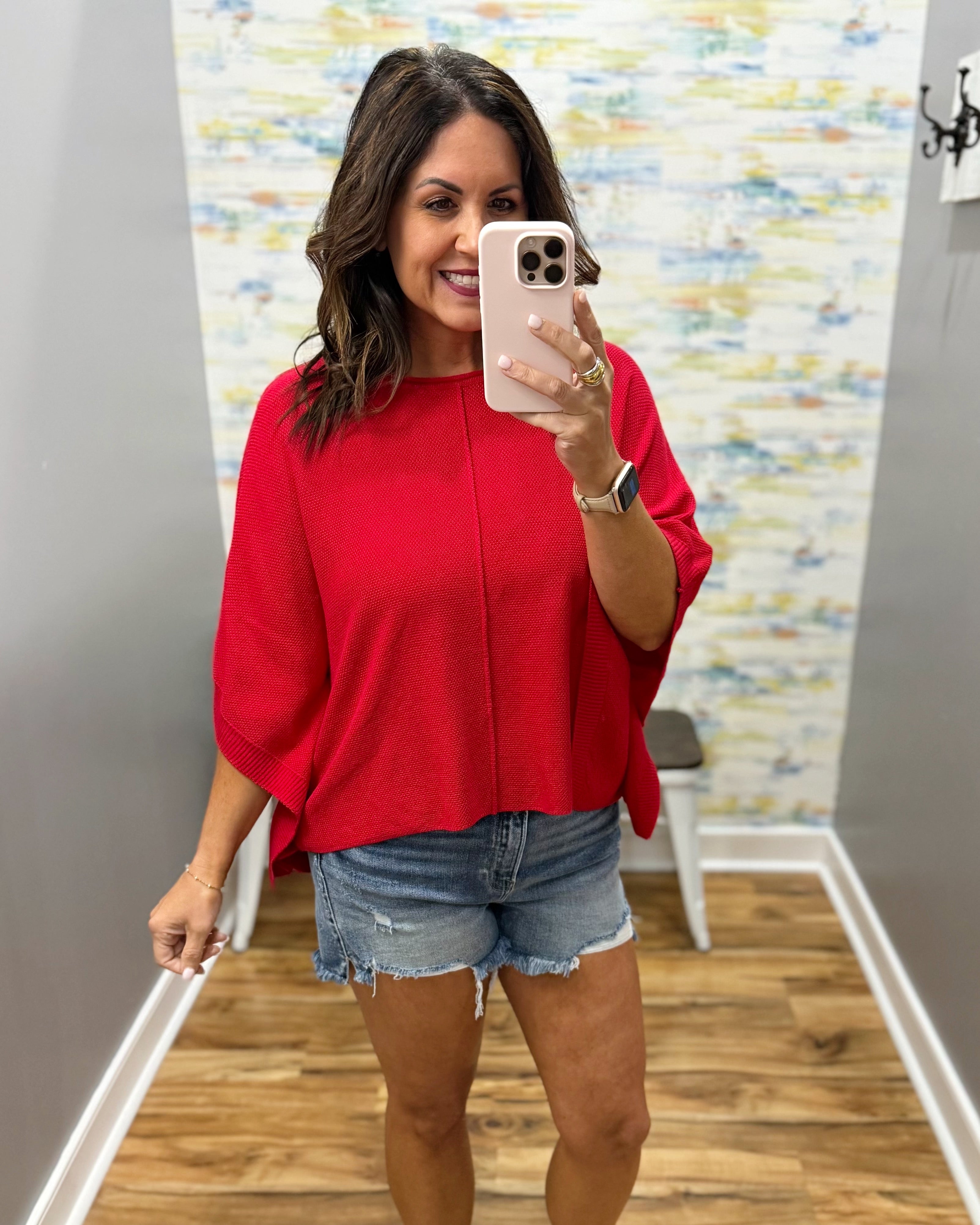 woman wearing a red dolman top with denim shorts.