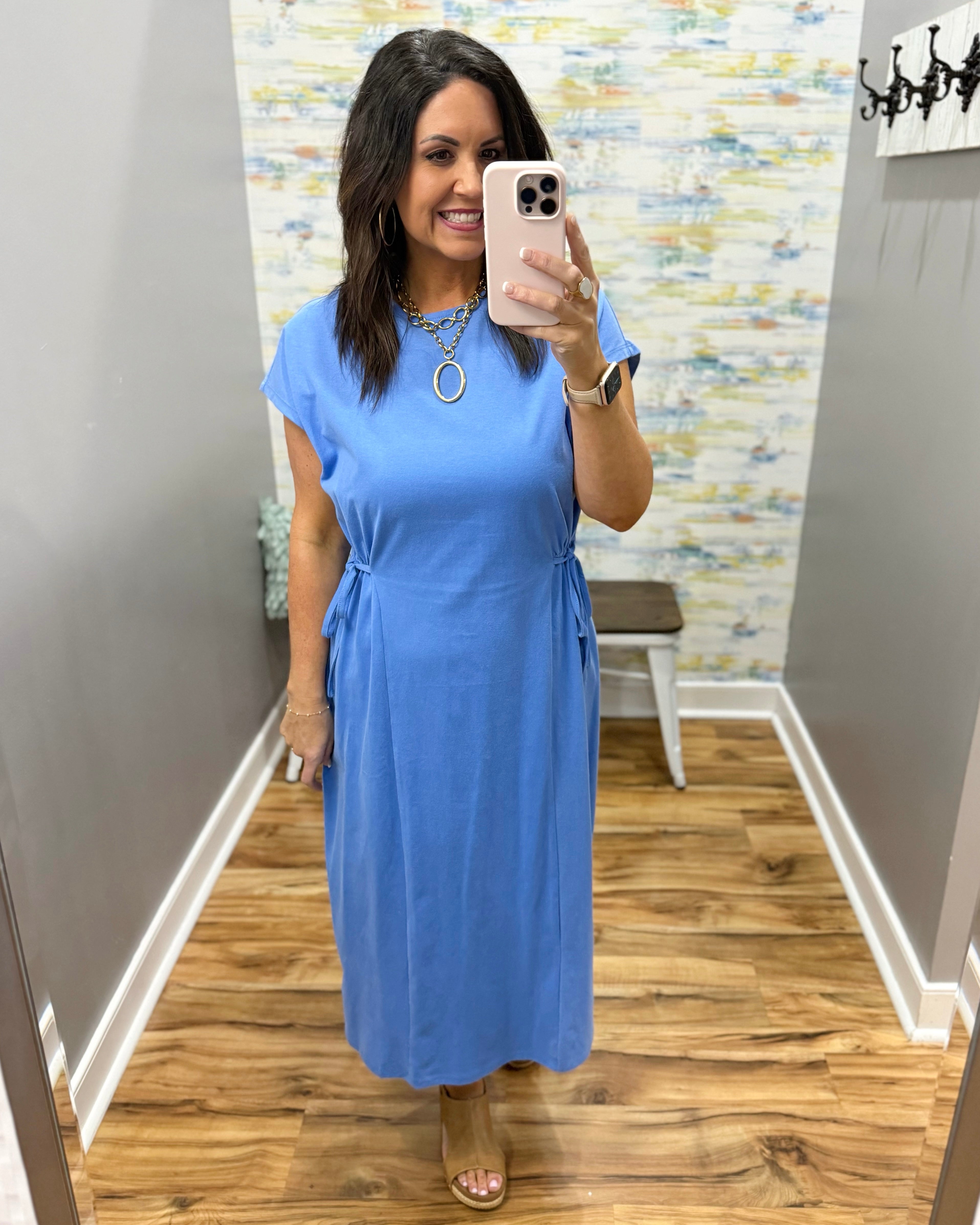 Woman wearing a blue dress in a room with patterned wallpaper.