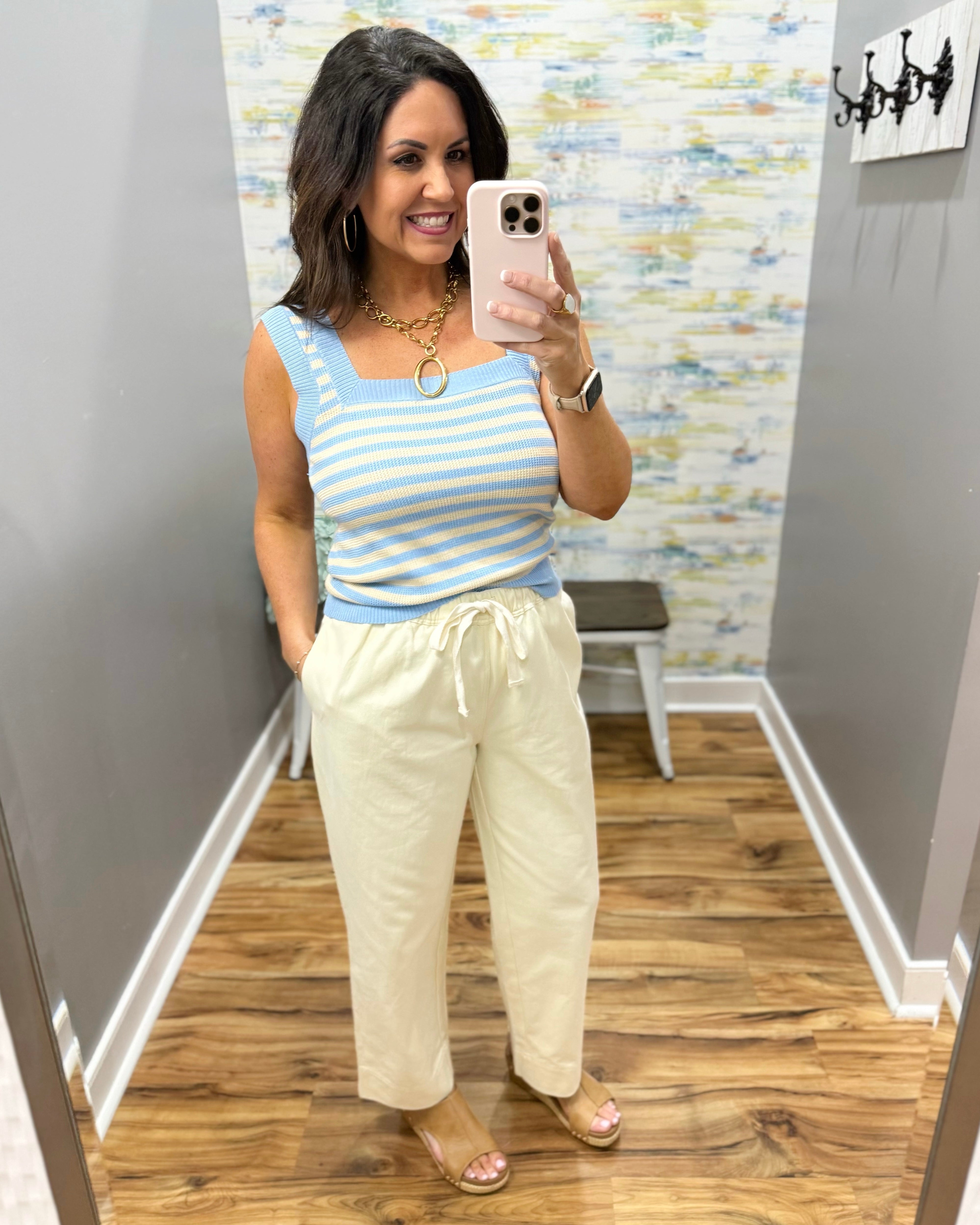 Woman wearing a striped tank top and light-colored pants in a room with a textured wall.