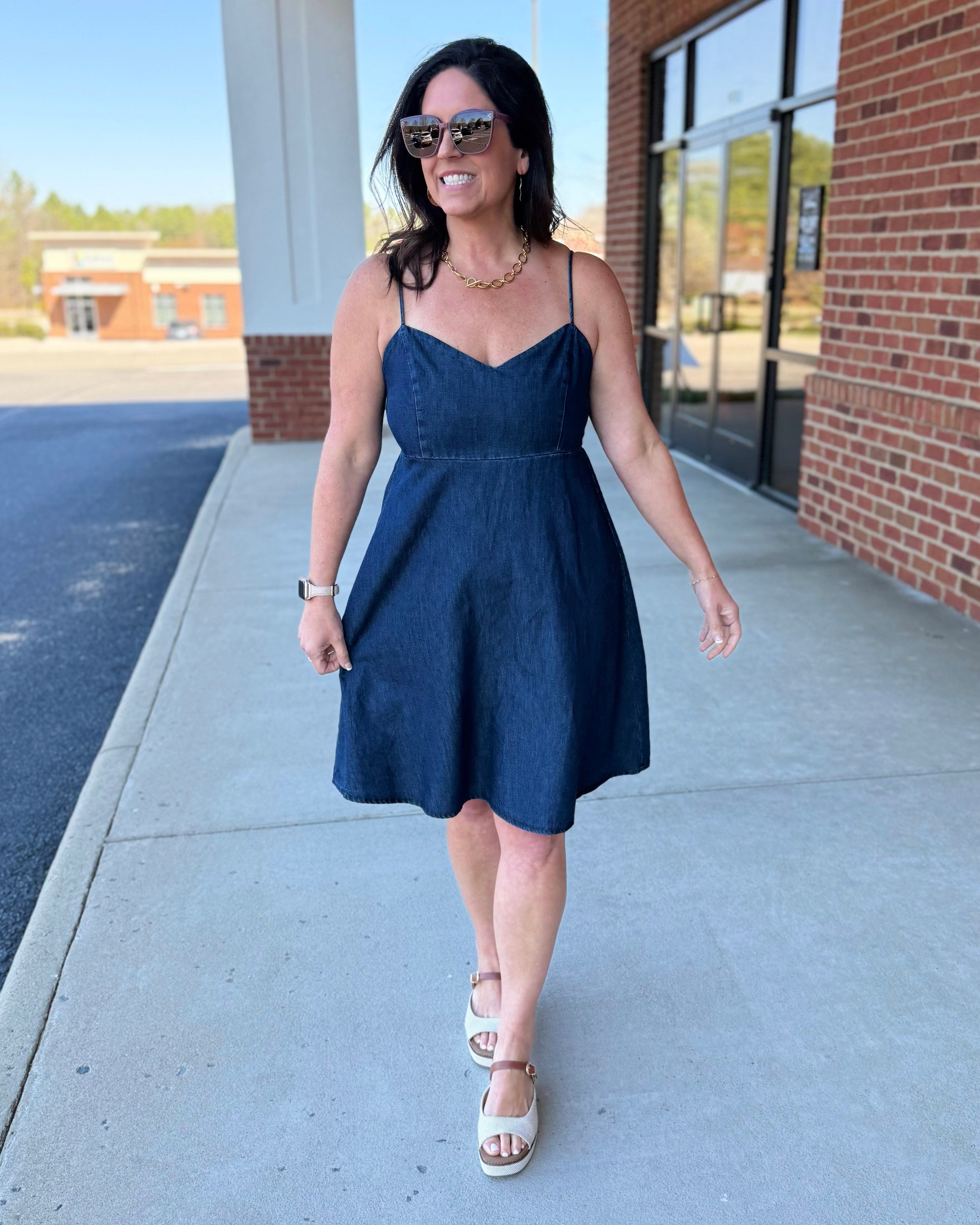 Woman in a blue dress walking on a sidewalk with a building in the background
