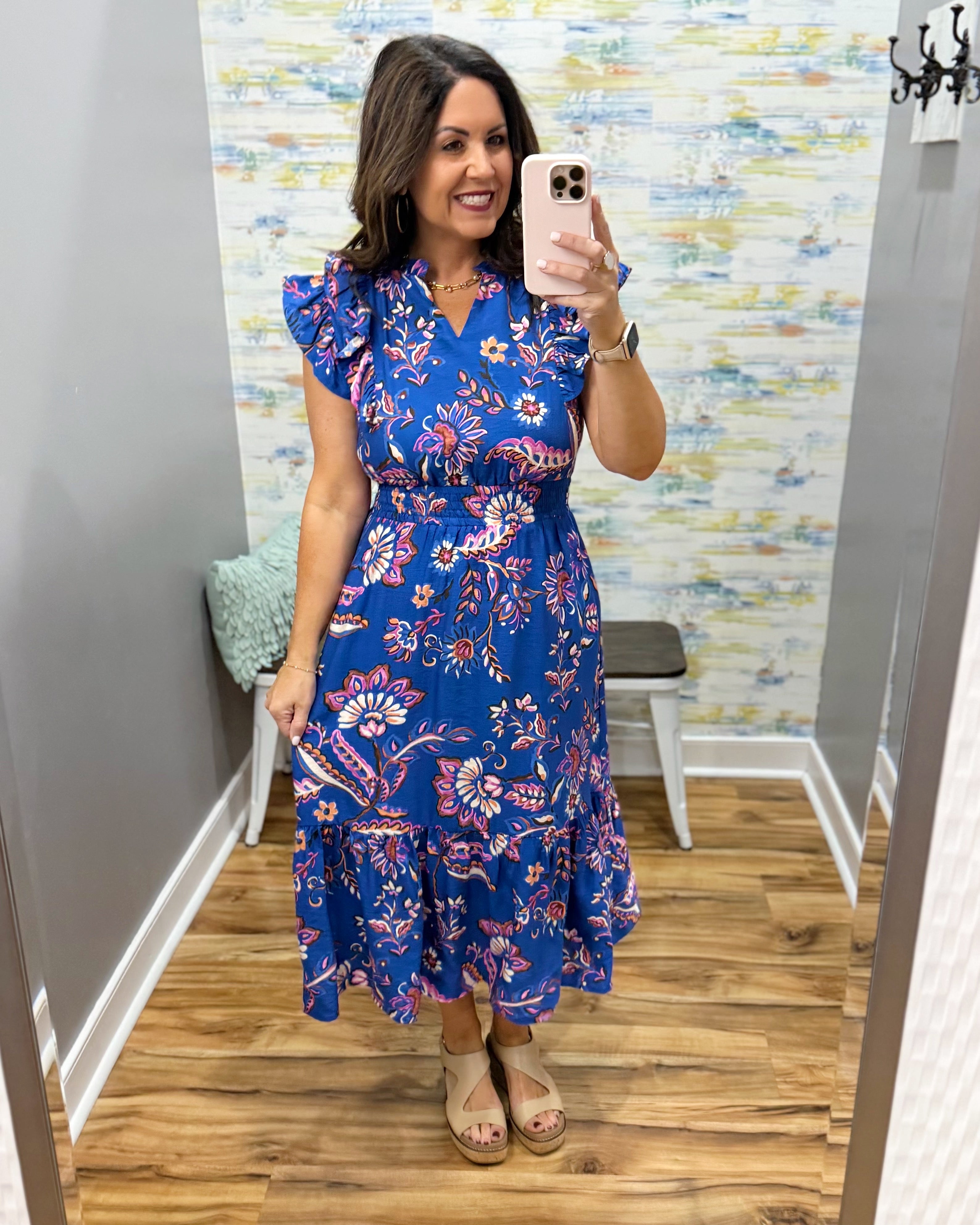 Woman taking a mirror selfie wearing a blue floral dress in a room with colorful wallpaper.