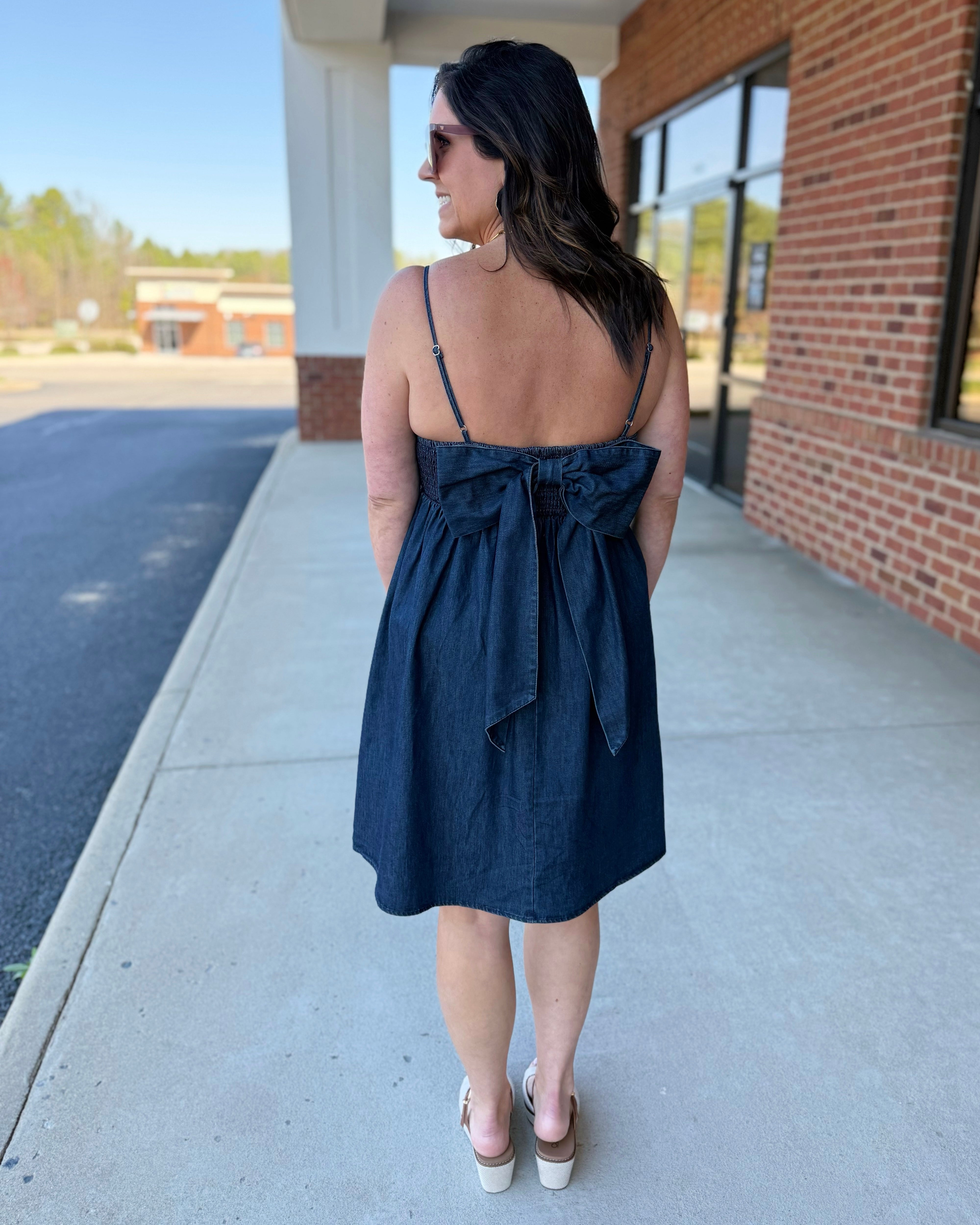 Woman wearing a navy blue dress with a tie detail on a sidewalk.