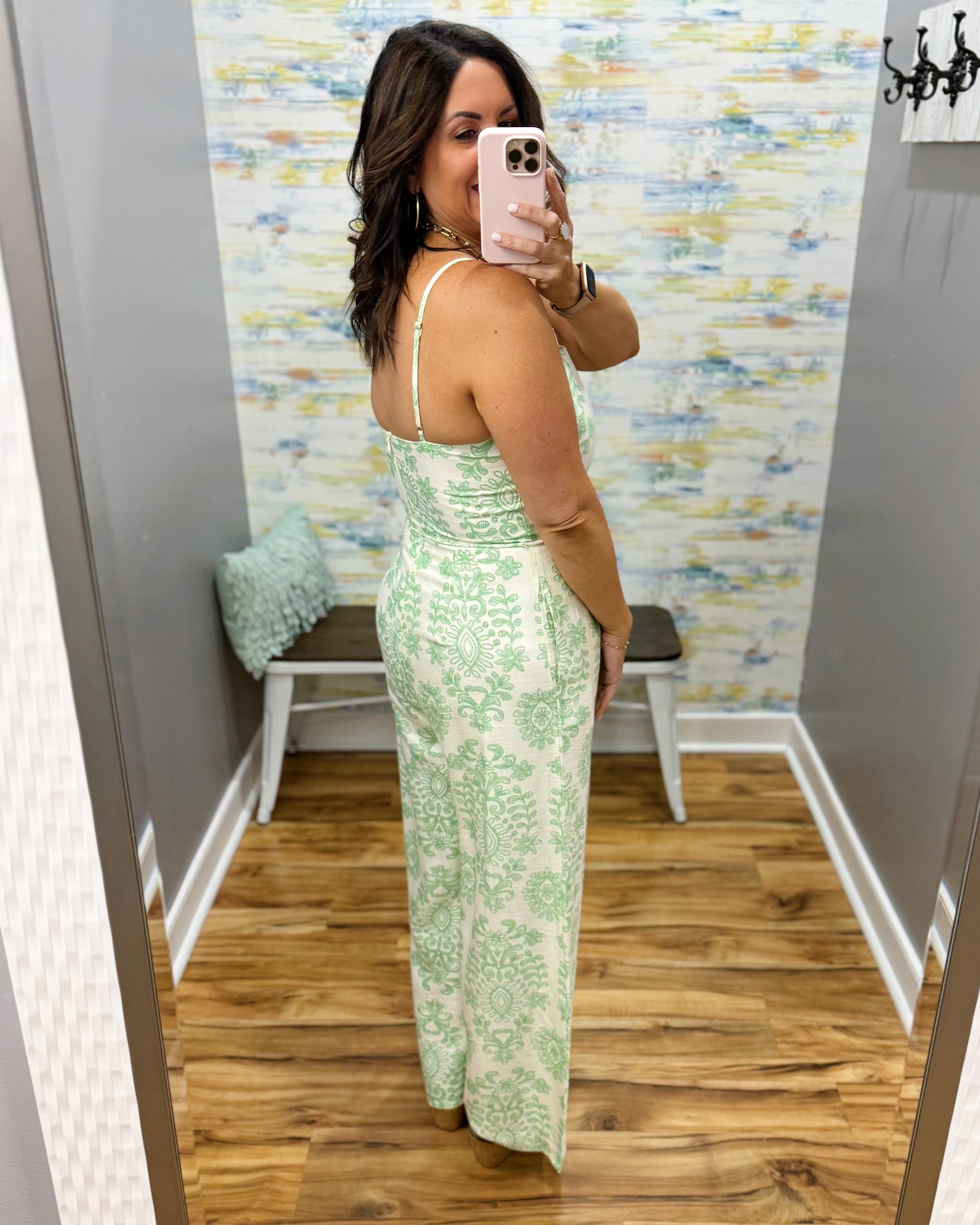 Woman taking a mirror selfie wearing a green floral dress in a room with patterned wallpaper.