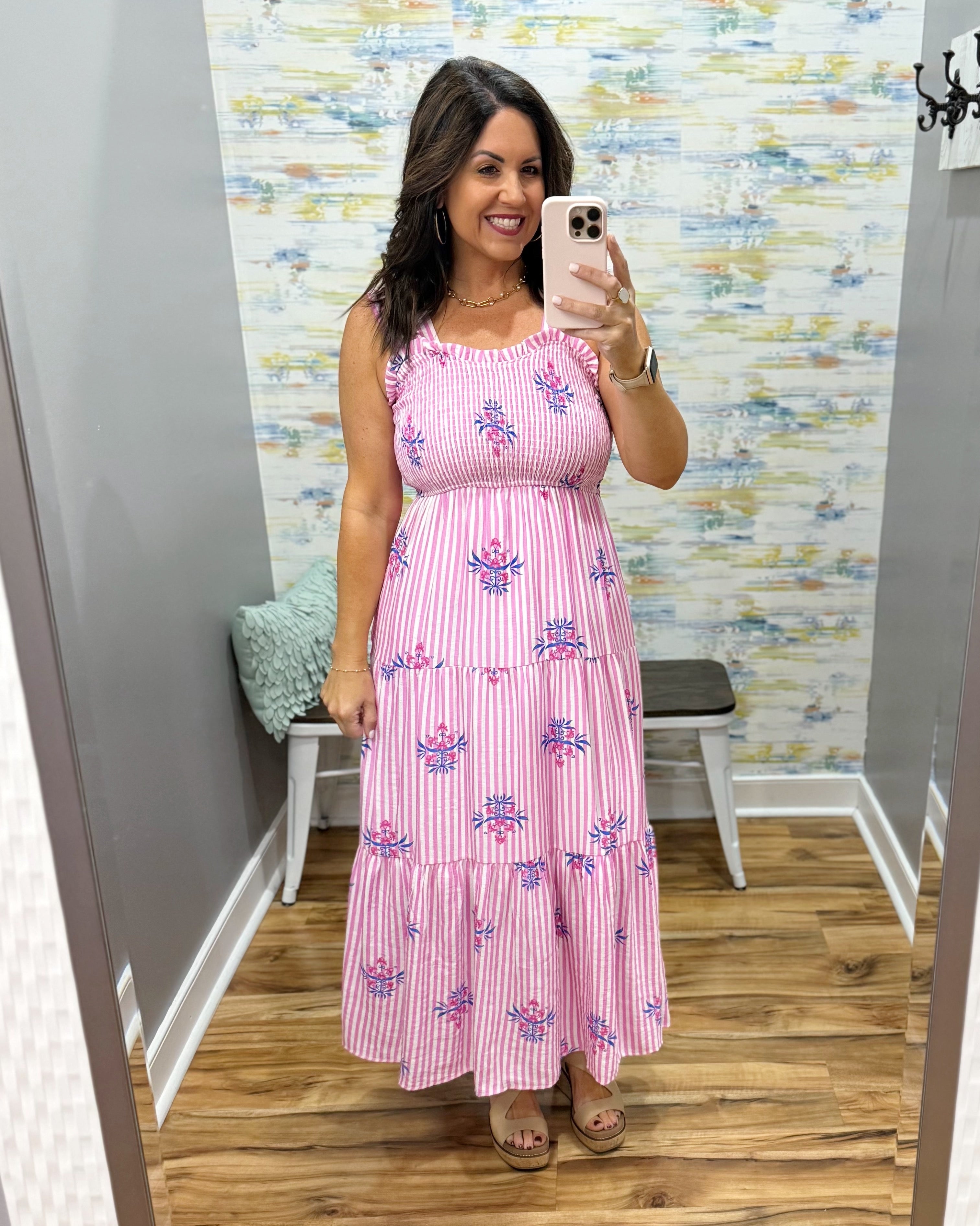 Woman taking a mirror selfie wearing a pink dress with floral patterns in a room with a patterned wall.