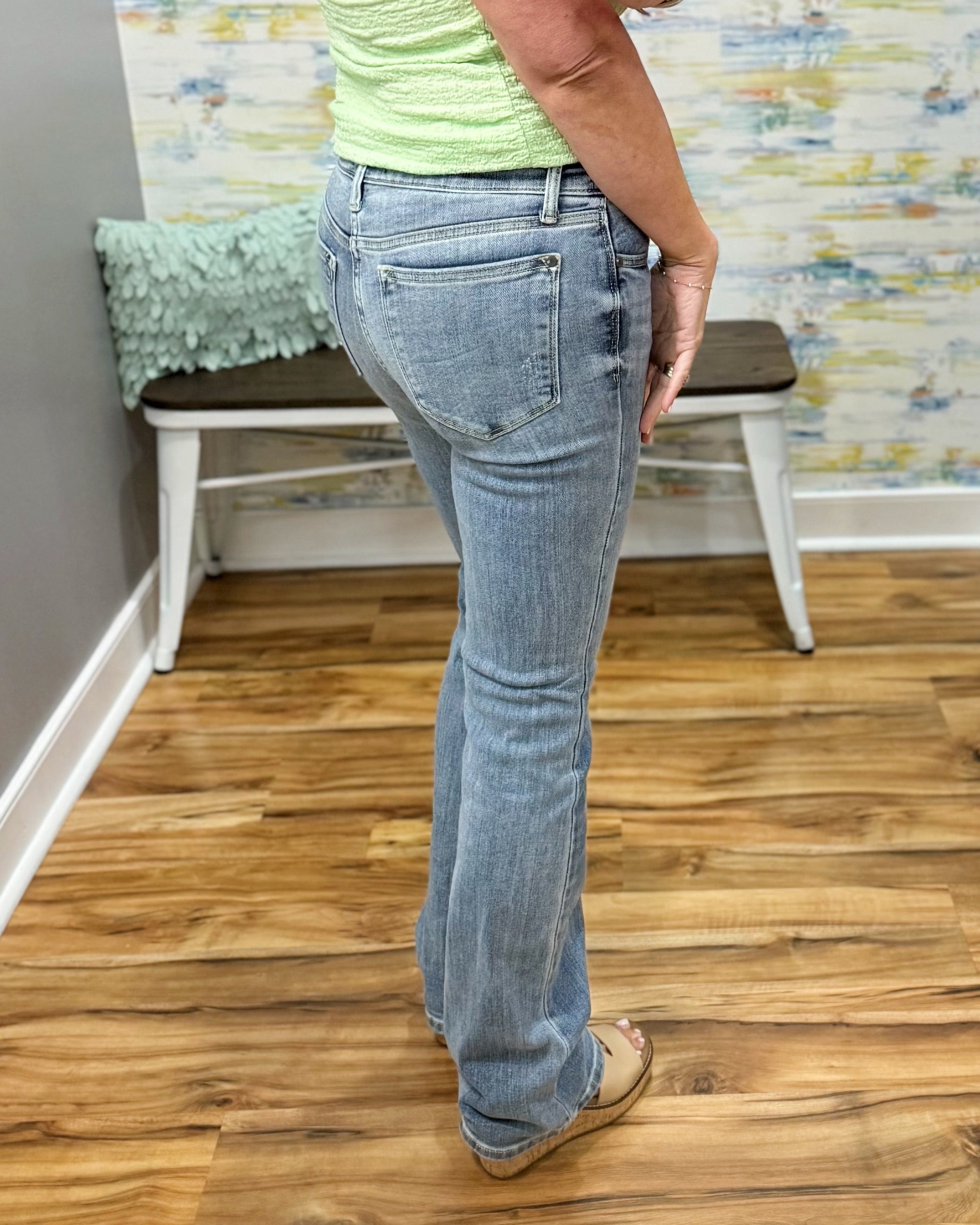 Person wearing blue jeans standing on a wooden floor with a colorful wall and chair in the background.