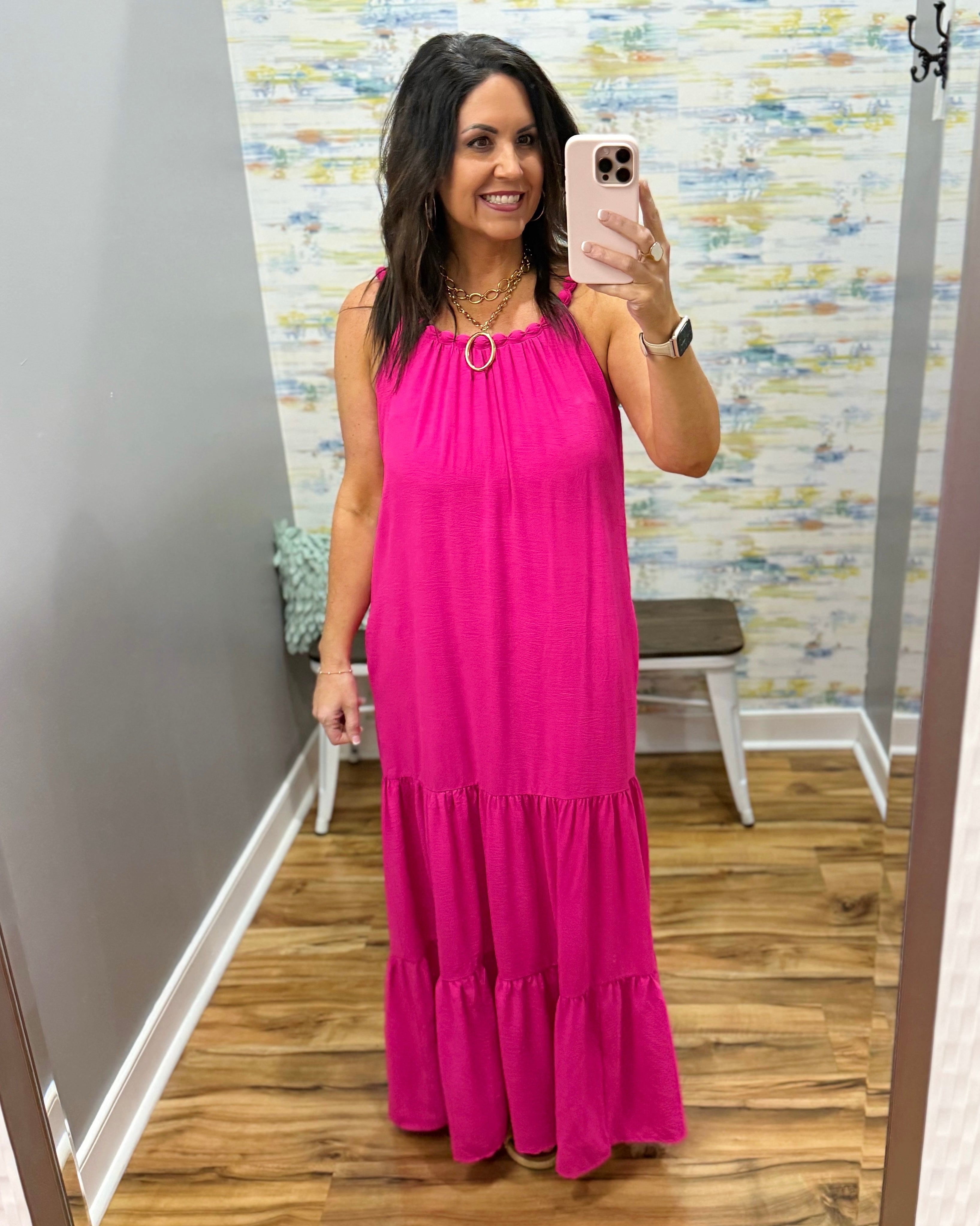 Woman wearing a pink dress taking a mirror selfie in a room with a colorful wall.