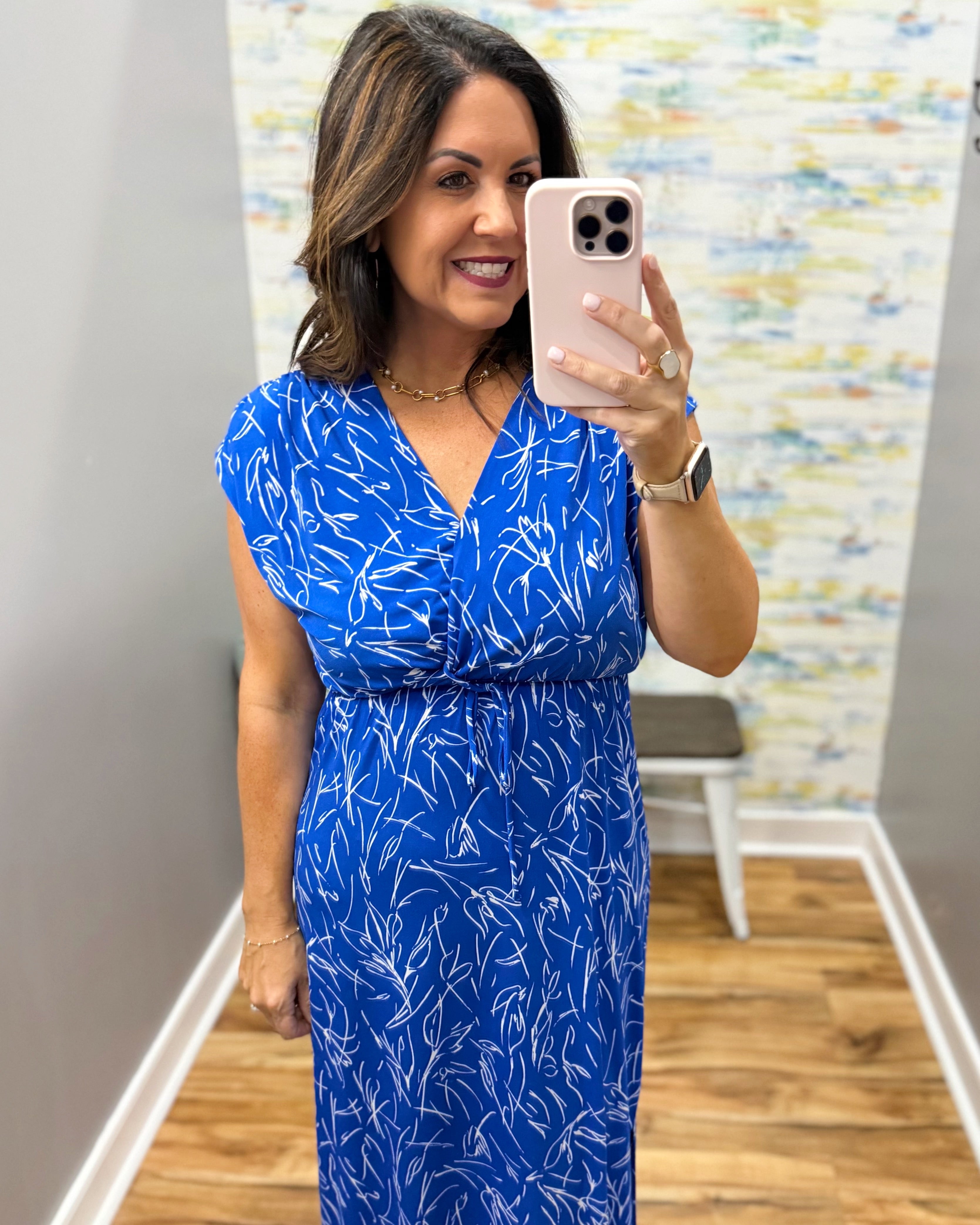 Woman taking a mirror selfie wearing a blue dress with a white pattern.