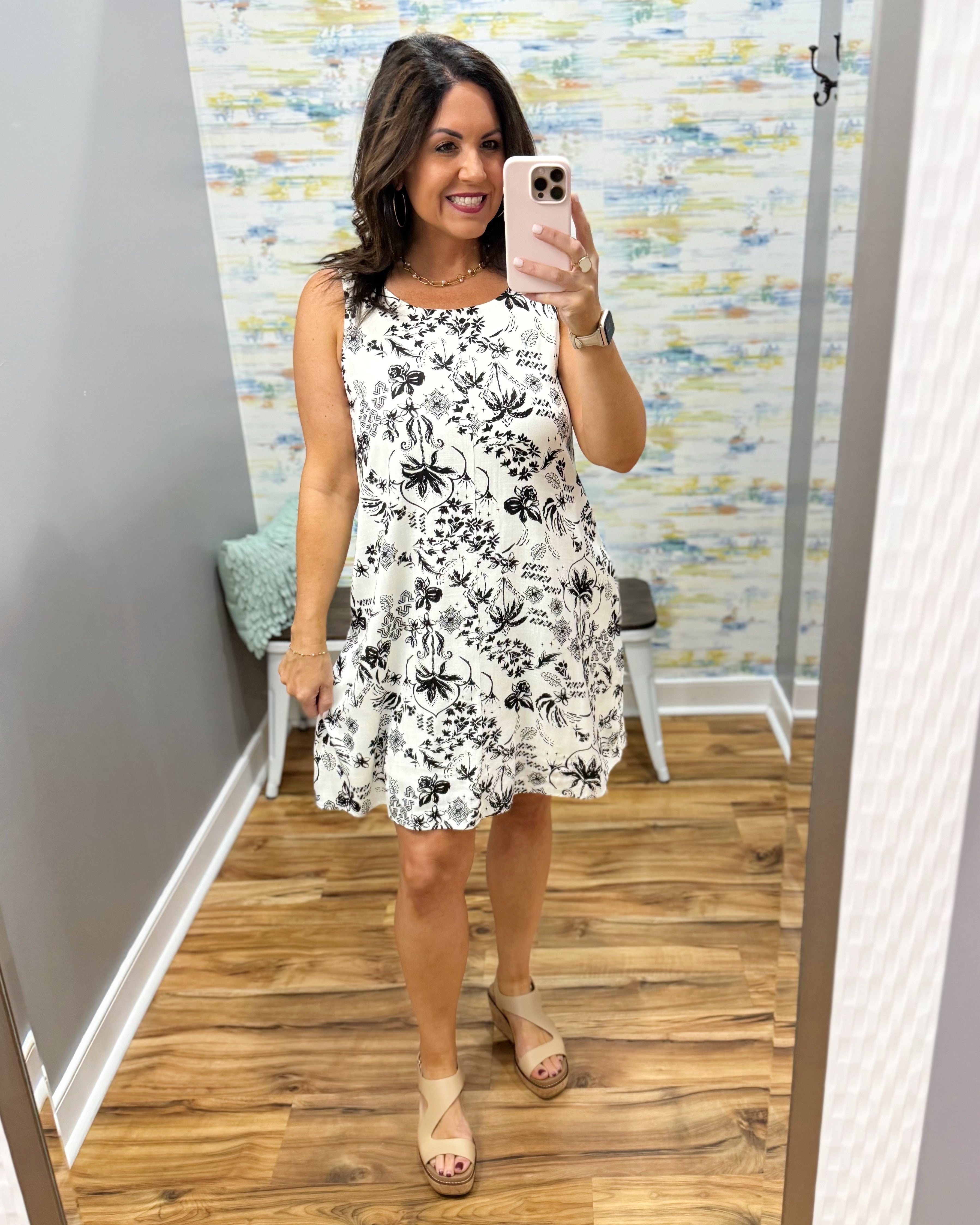 Woman taking a mirror selfie wearing a floral dress in a room with a colorful wall.