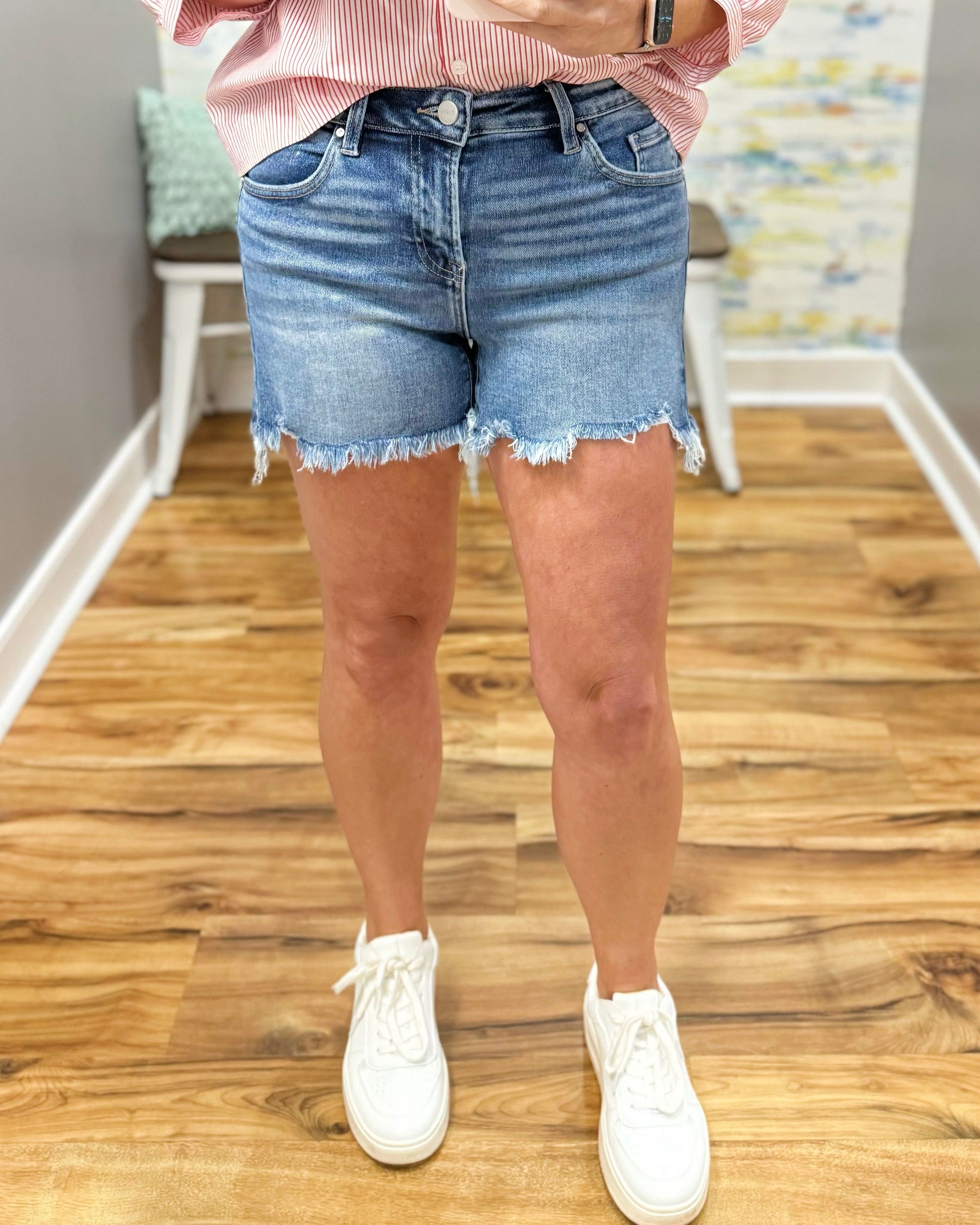 Person wearing light blue denim shorts and white sneakers on a wooden floor.