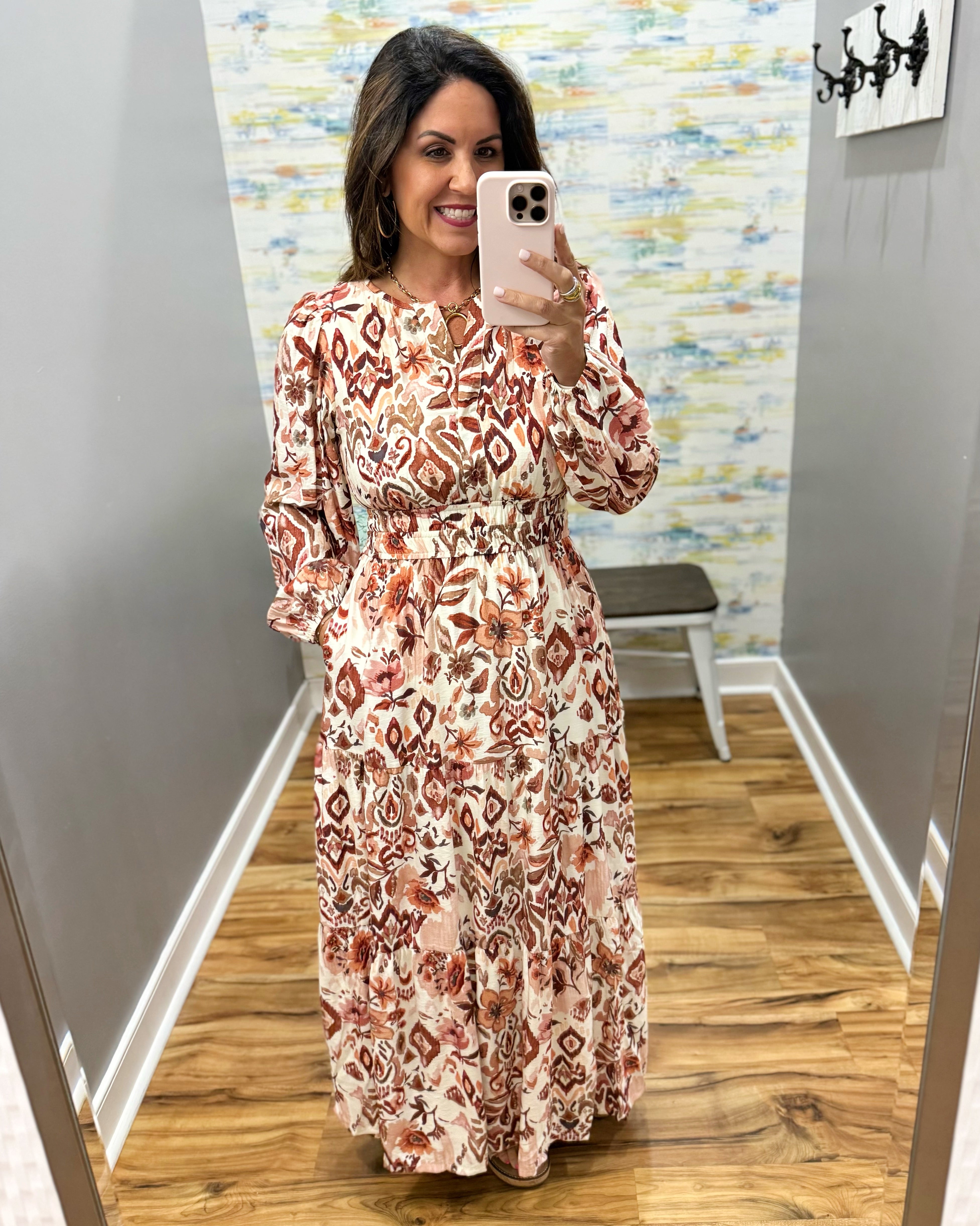 A woman takes a mirror selfie wearing a long-sleeve maxi dress with a bohemian-style geometric pattern in rust red, brown, and beige on a cream background.