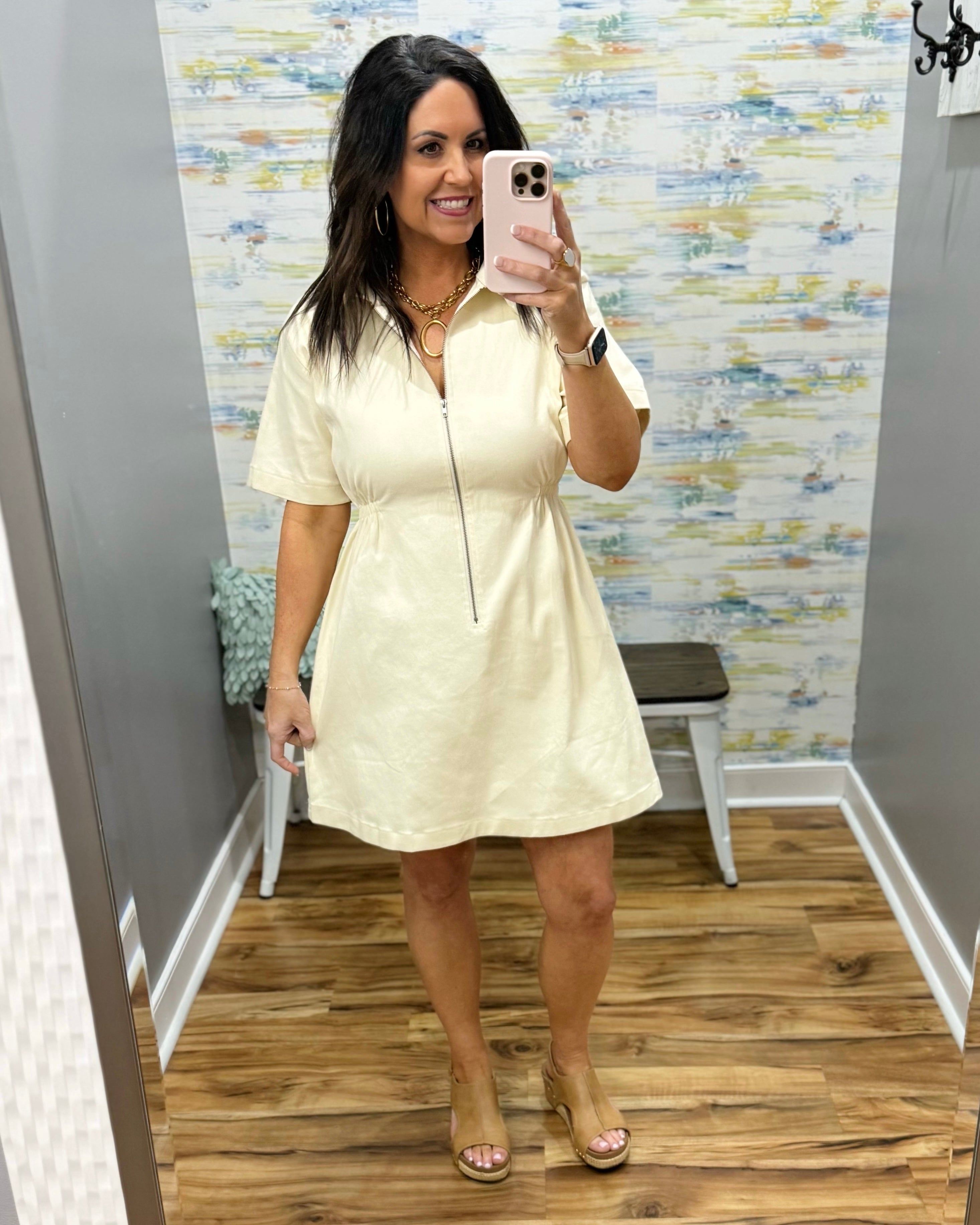 Woman wearing a beige dress in a room with a patterned wall.