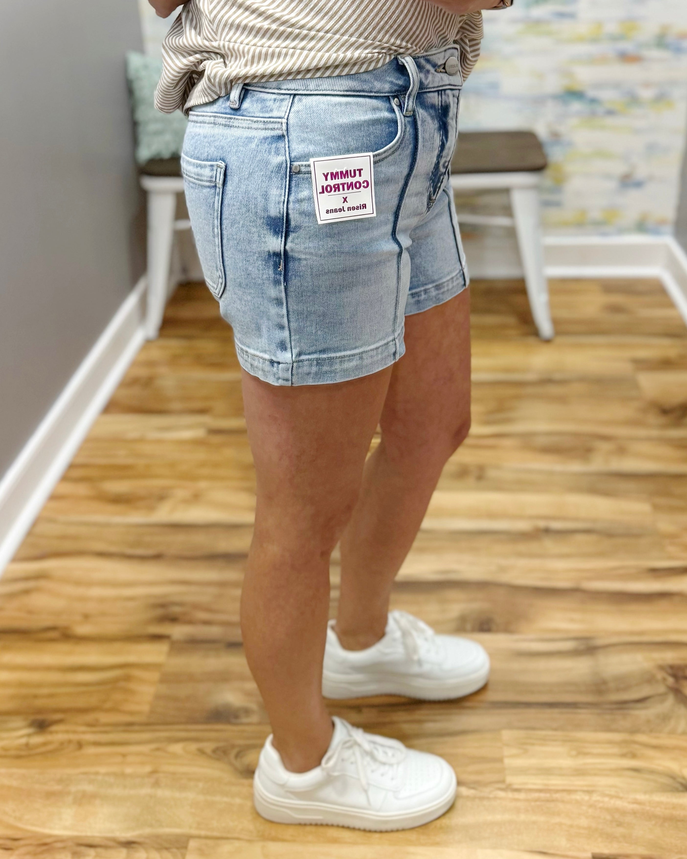 Person wearing light blue denim shorts with a visible brand label on a wooden floor.