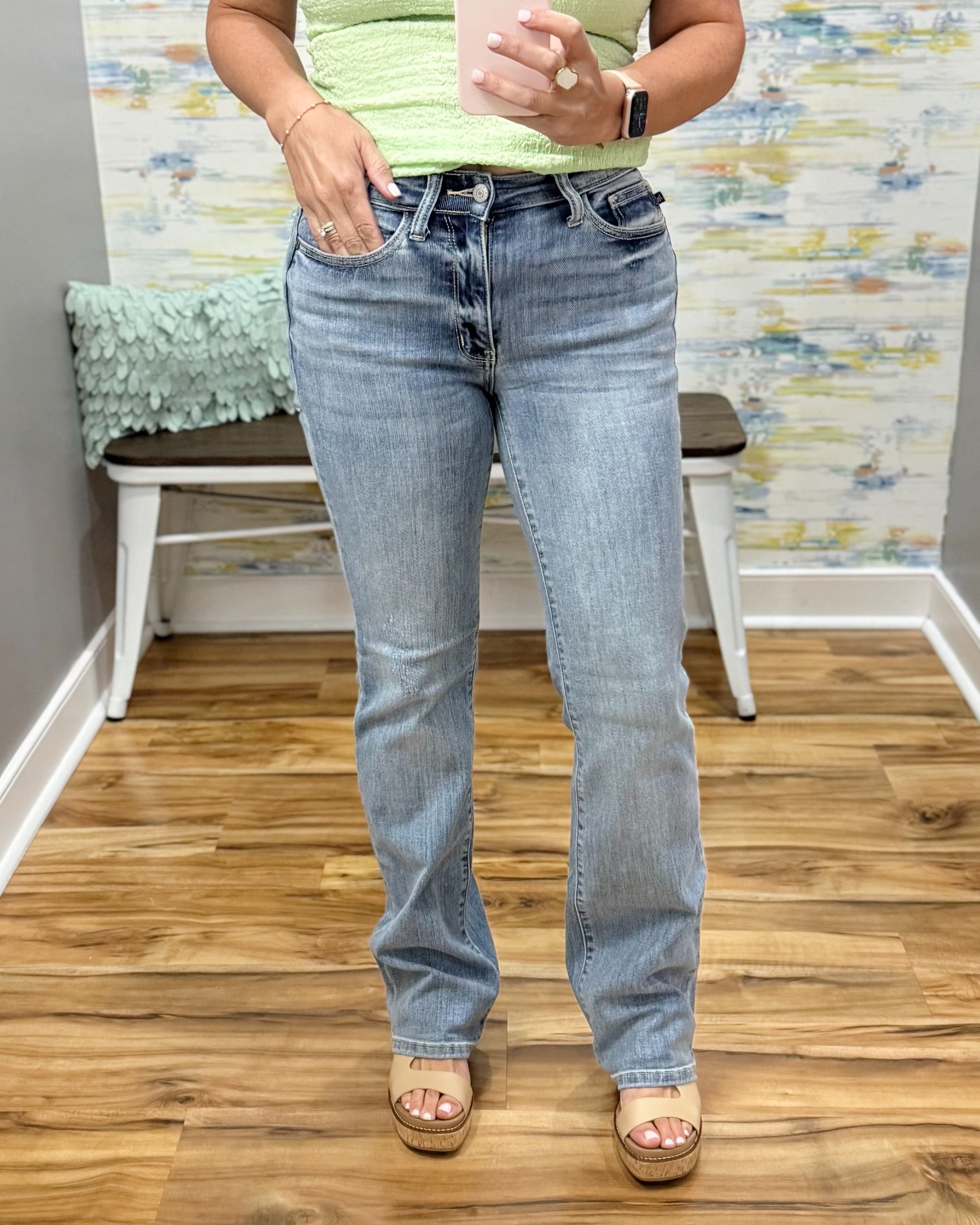 Person wearing light blue jeans standing on a wooden floor with a colorful wall in the background.