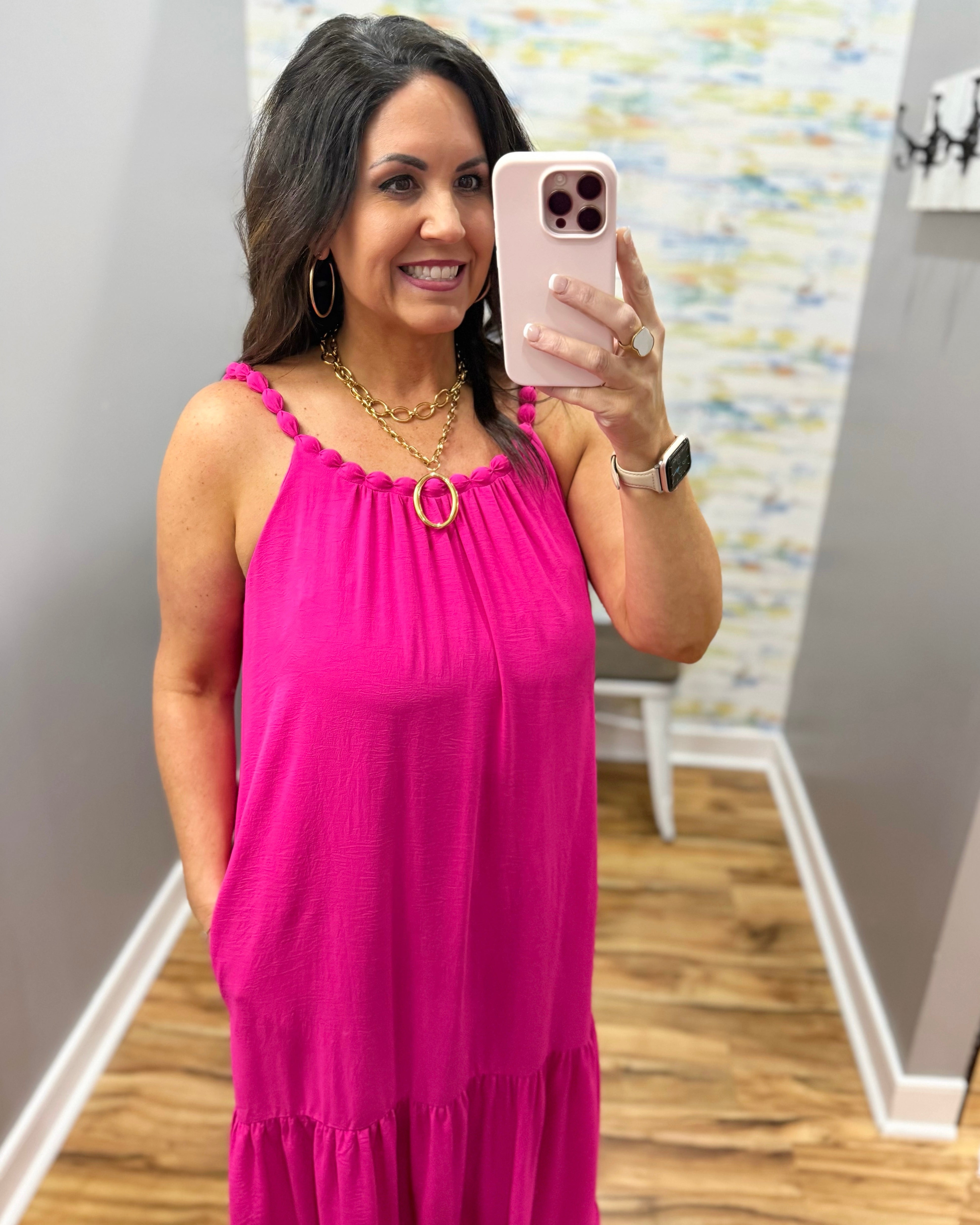 Woman in a pink dress taking a mirror selfie in a room with a colorful wall.