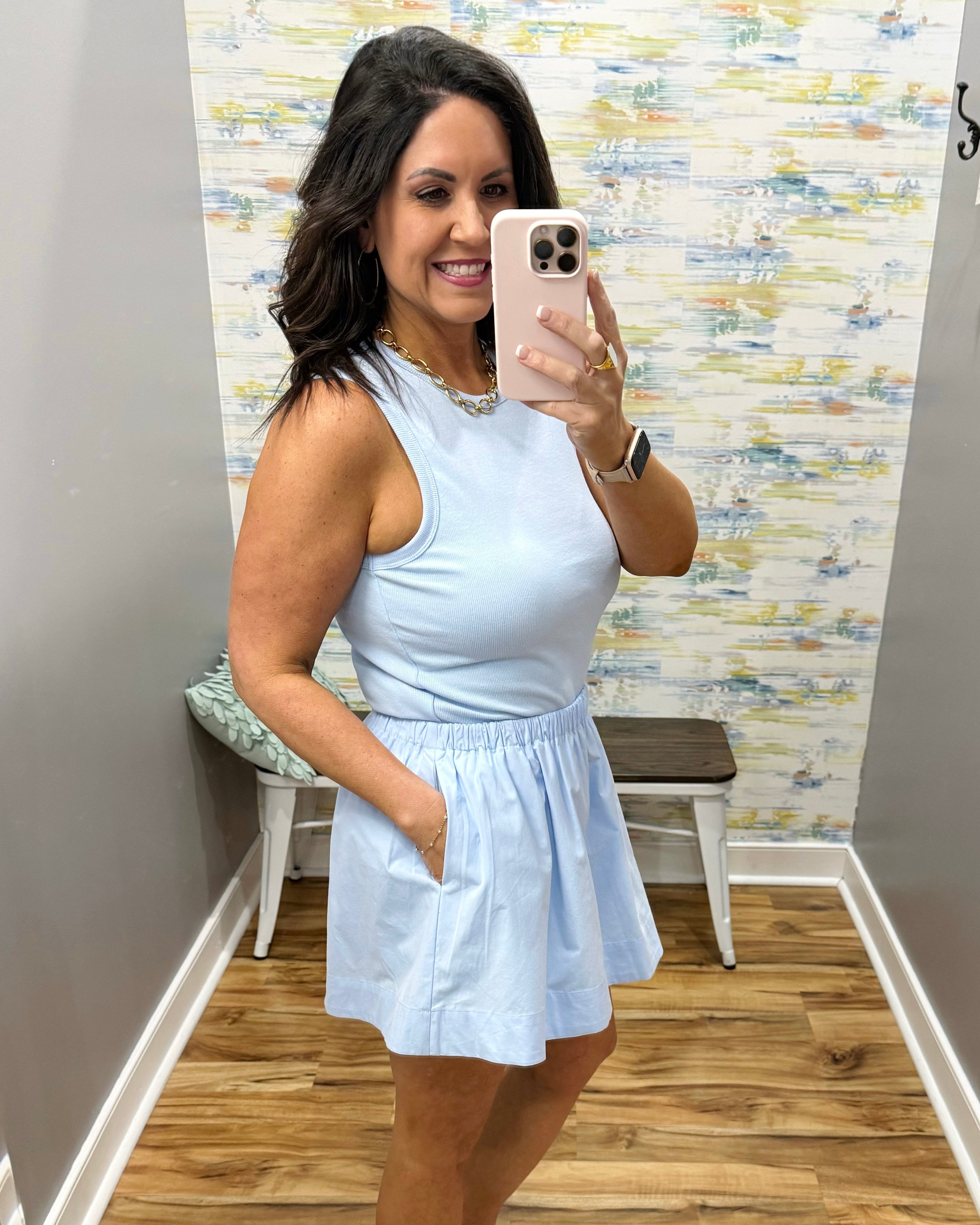 Woman taking a mirror selfie wearing a light blue dress in a room with a textured wall.
