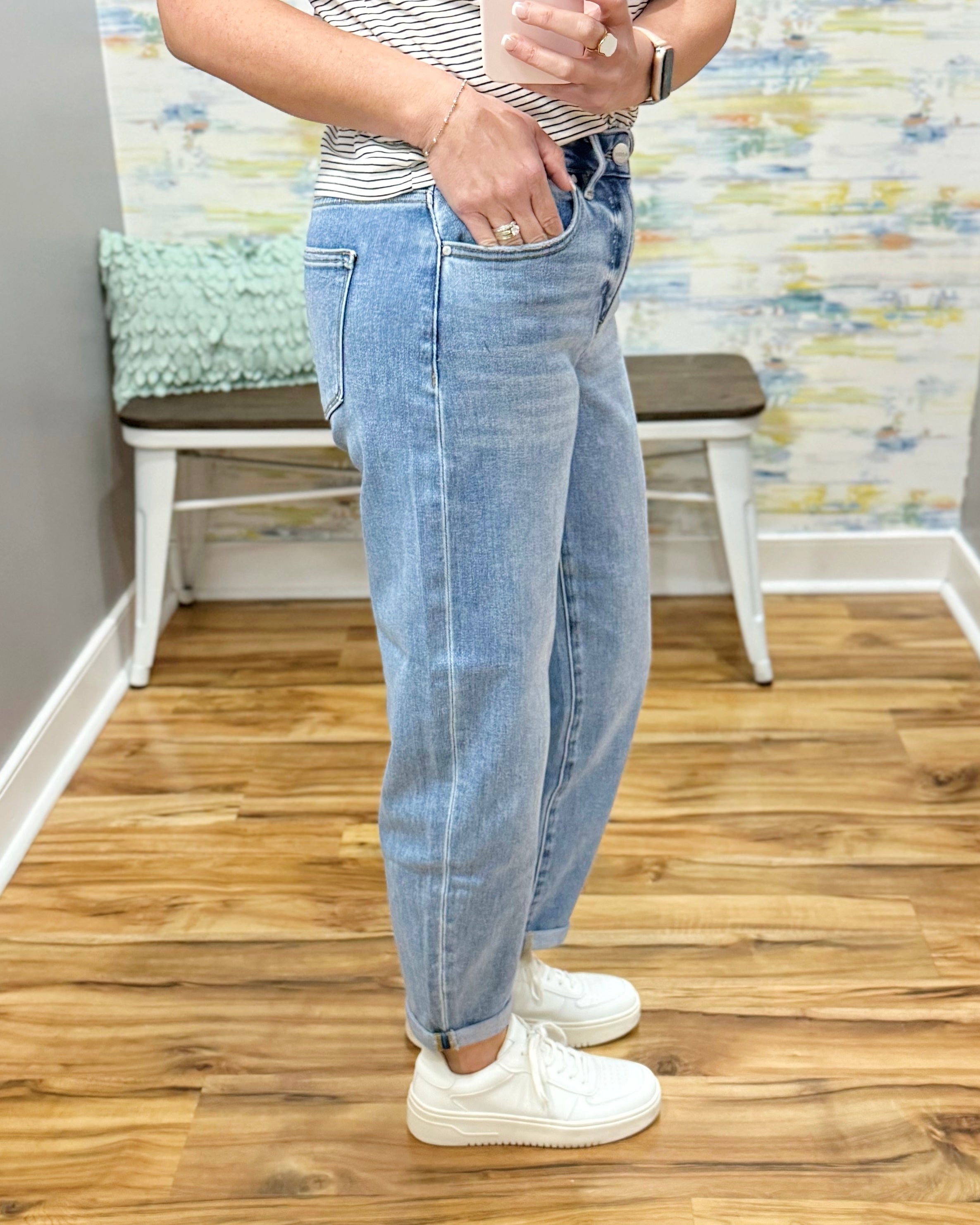 Person wearing light blue jeans and white sneakers in a room with wooden flooring and a colorful wall.