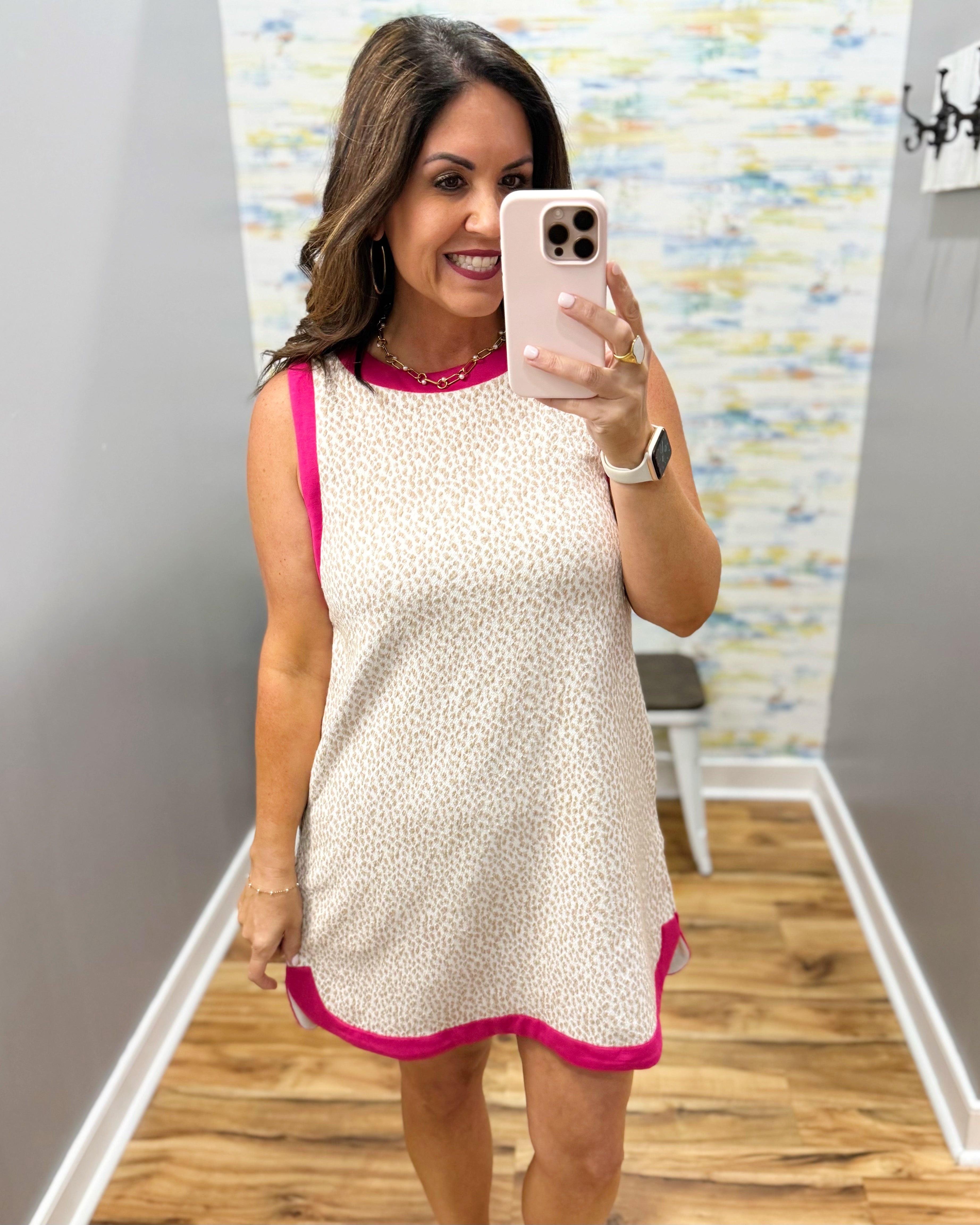 Woman taking a mirror selfie wearing a white dress with pink trim.