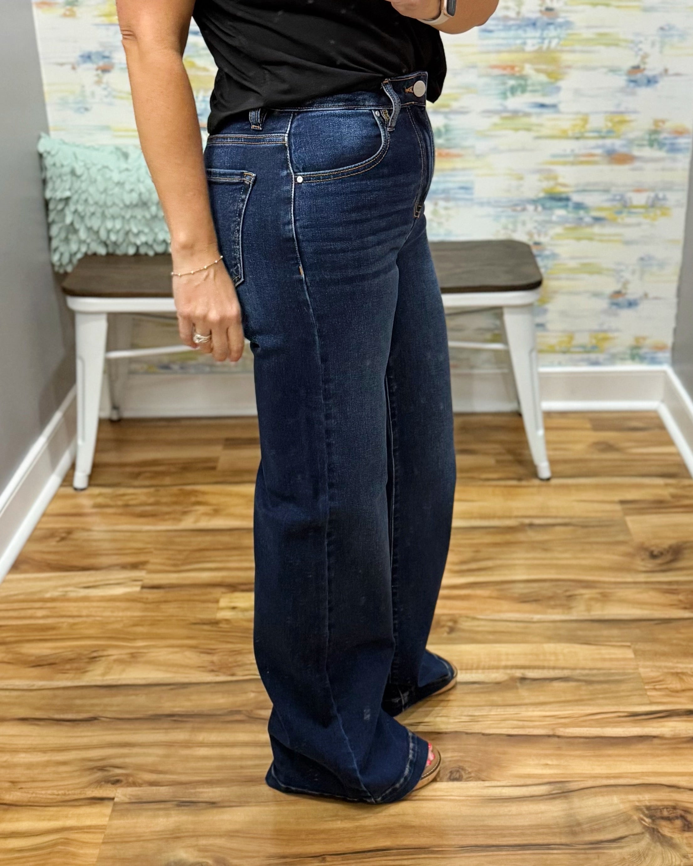 Person wearing blue jeans standing on a wooden floor with a colorful wall in the background.