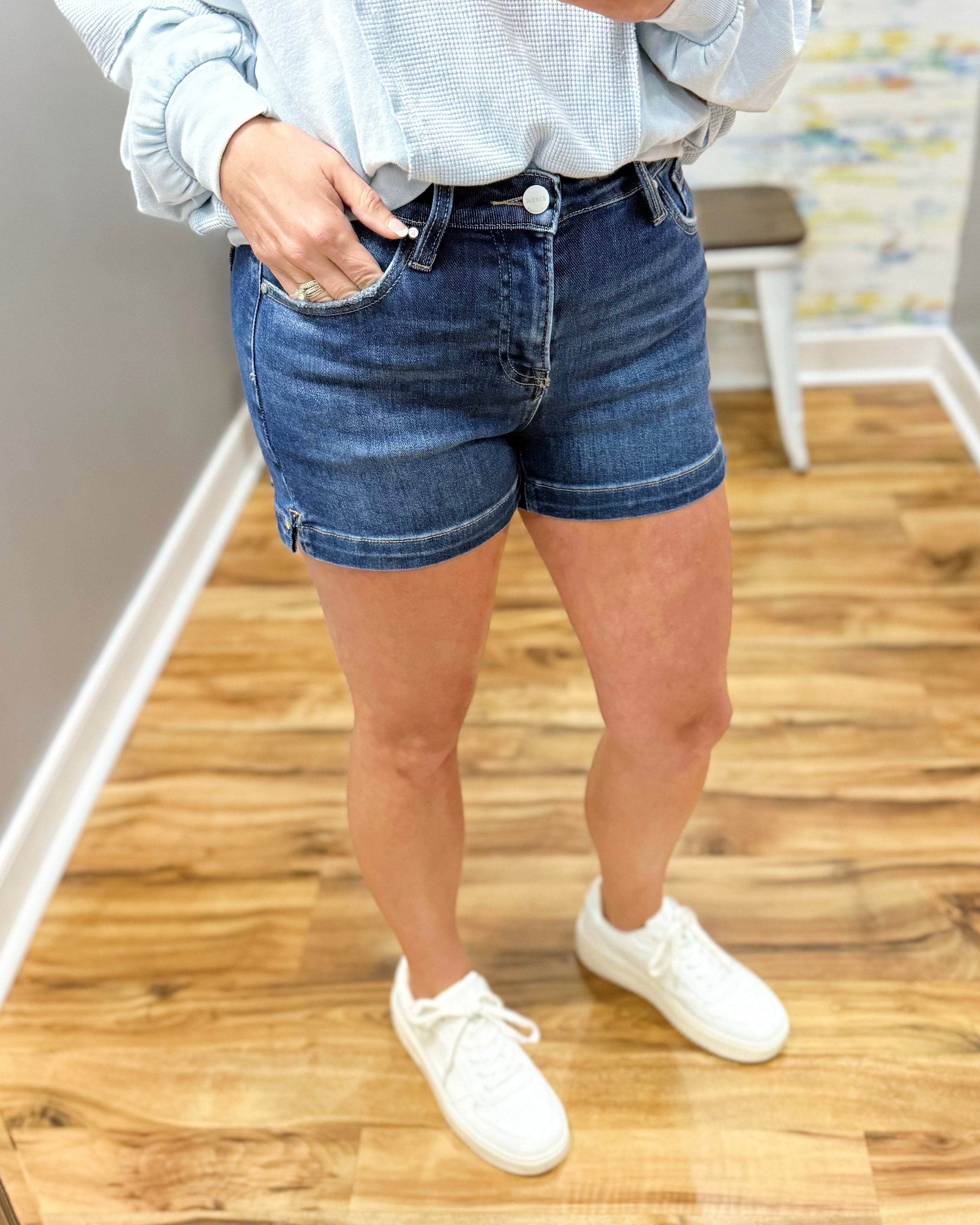 Person wearing blue denim shorts and white sneakers on a wooden floor.
