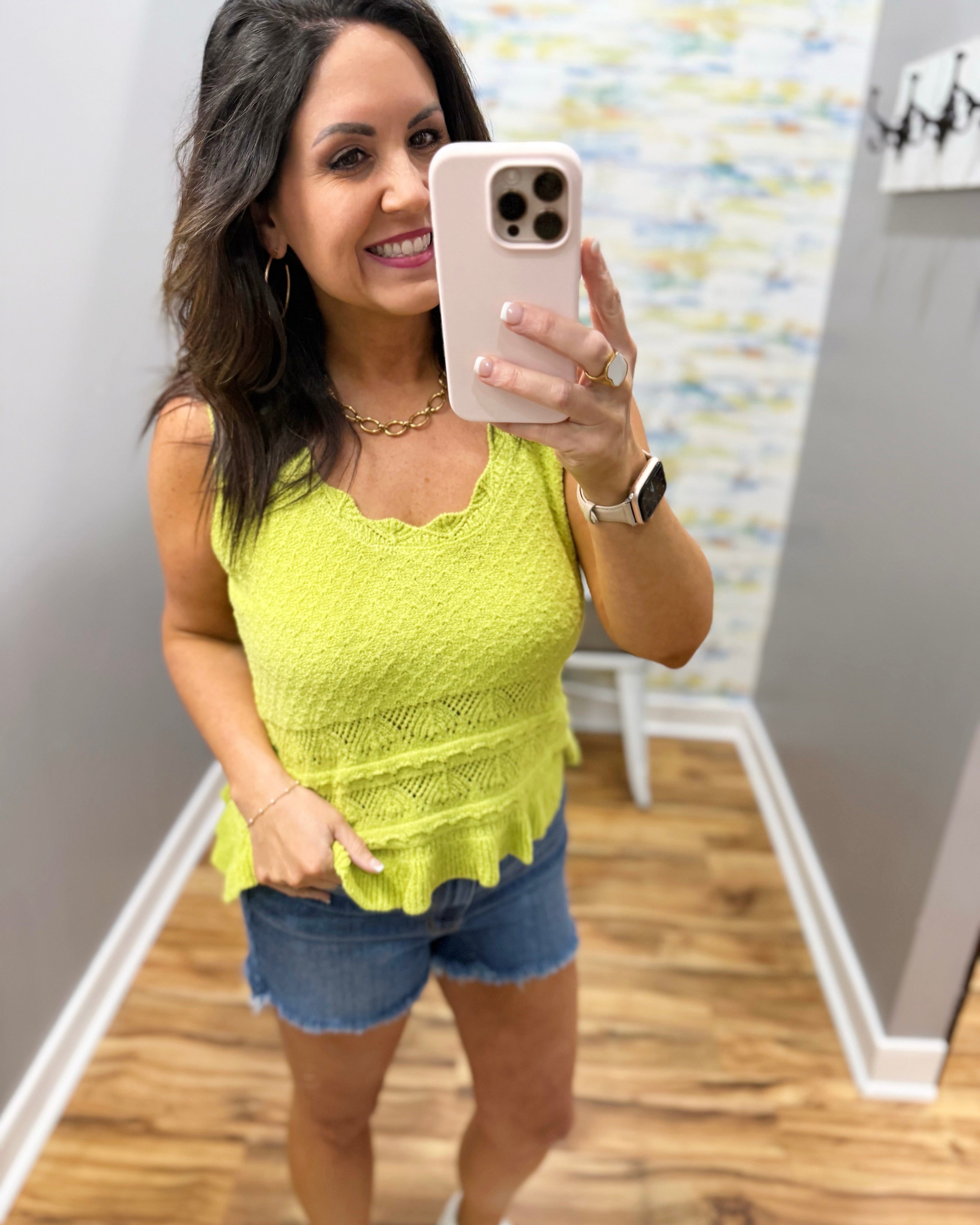 Woman taking a mirror selfie wearing a yellow top and denim shorts.