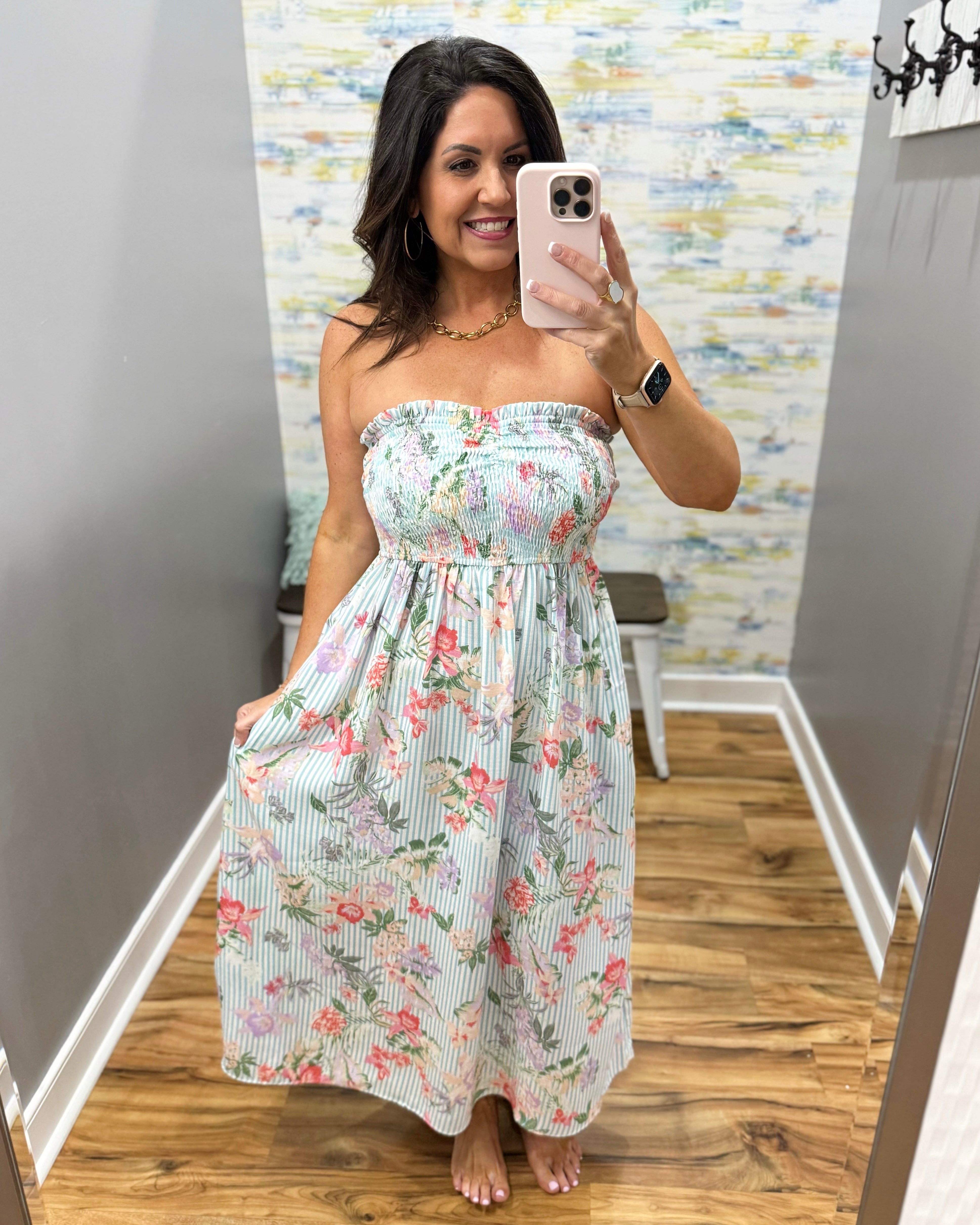 Woman taking a mirror selfie wearing a floral strapless dress in a room with a patterned wall.