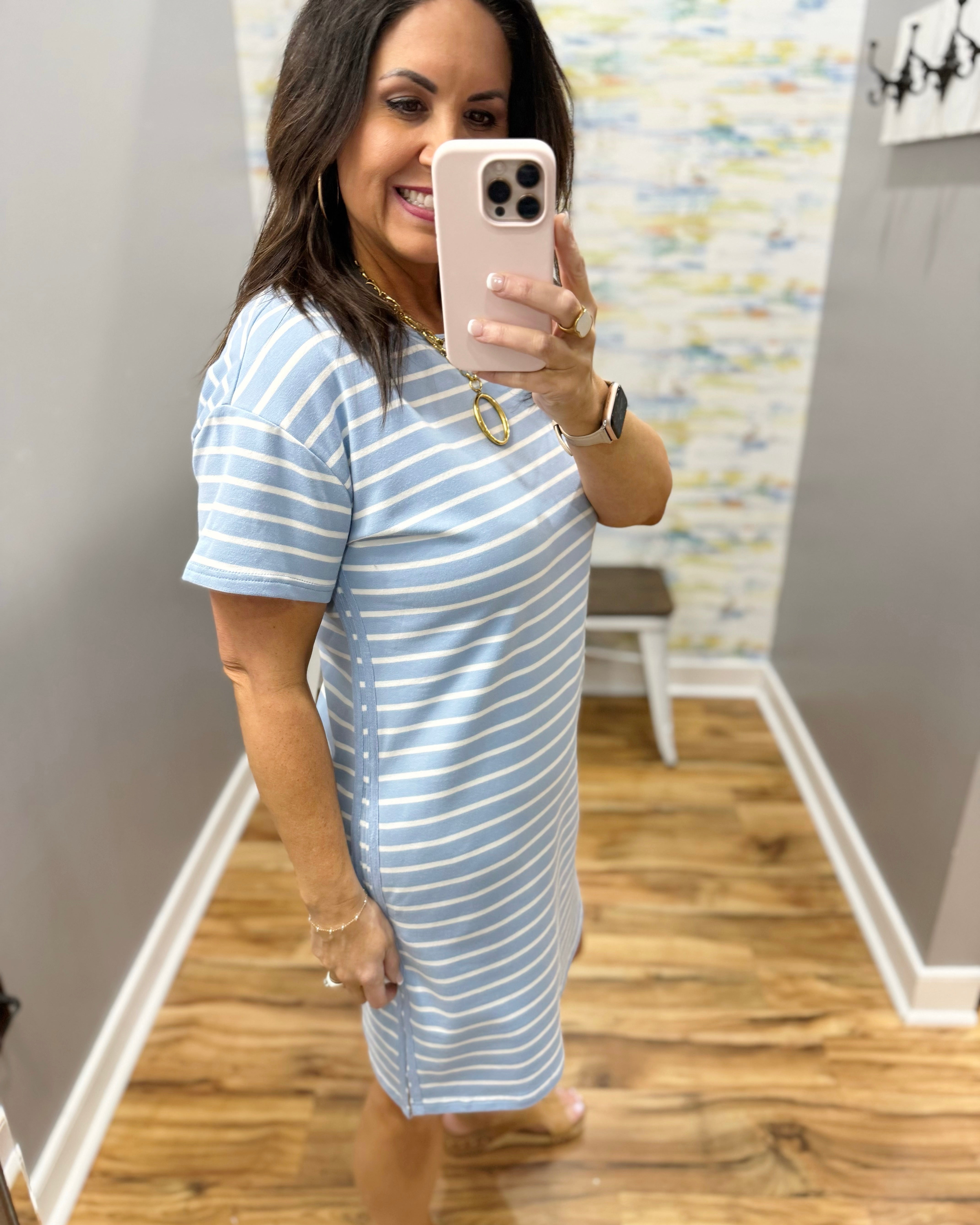 Woman wearing a blue and white striped dress in a room with wooden flooring and a colorful wall.