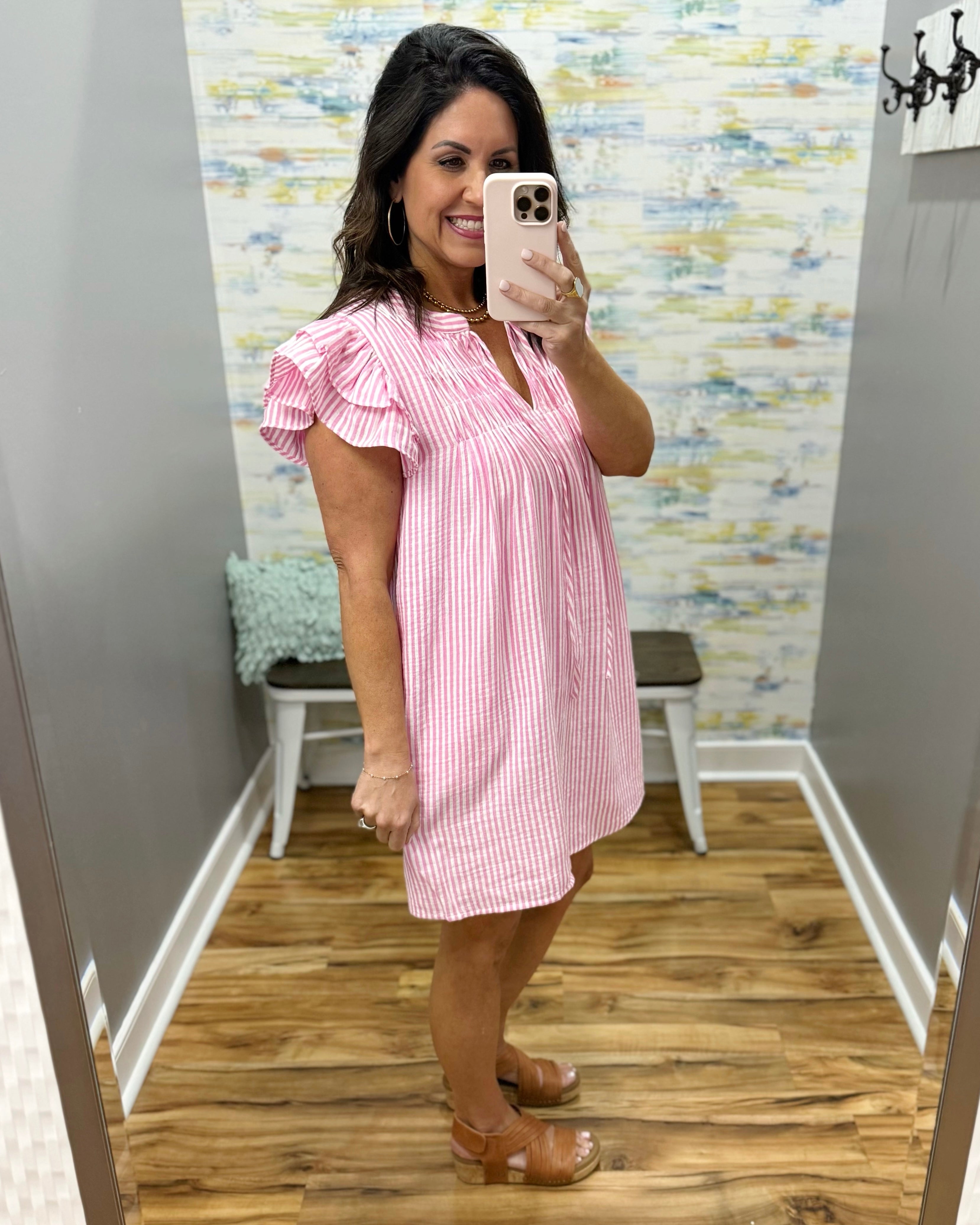 Woman taking a mirror selfie wearing a pink and white striped dress in a room with a colorful wall.