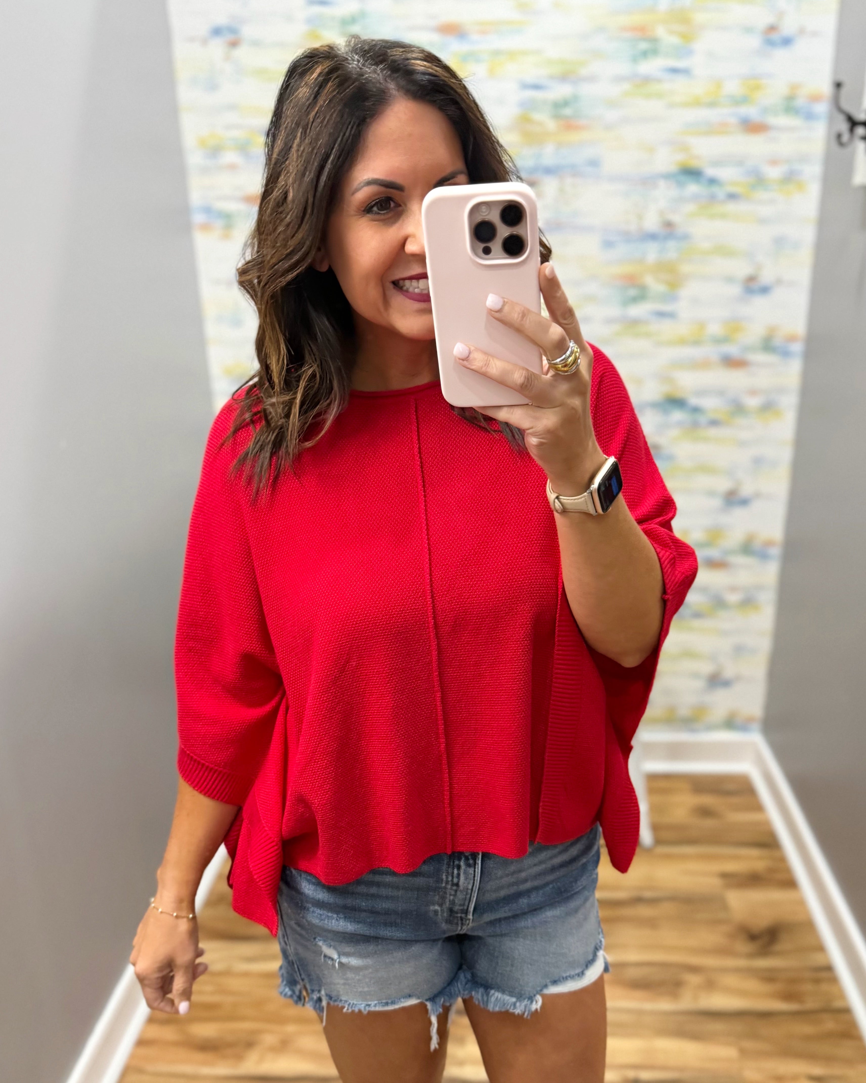 woman wearing a red dolman top and denim shorts.
